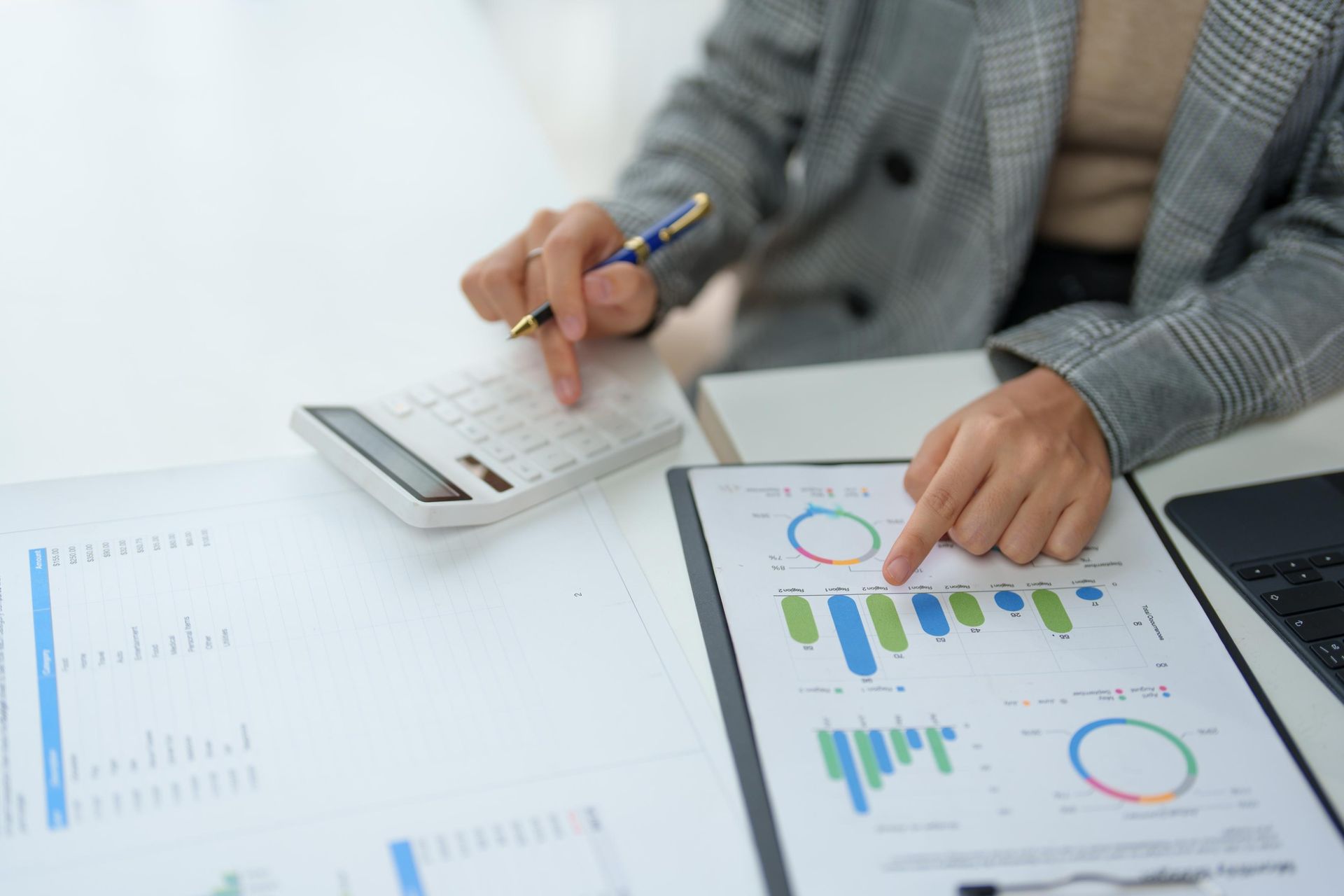 A woman is sitting at a desk using a calculator and a pen.
