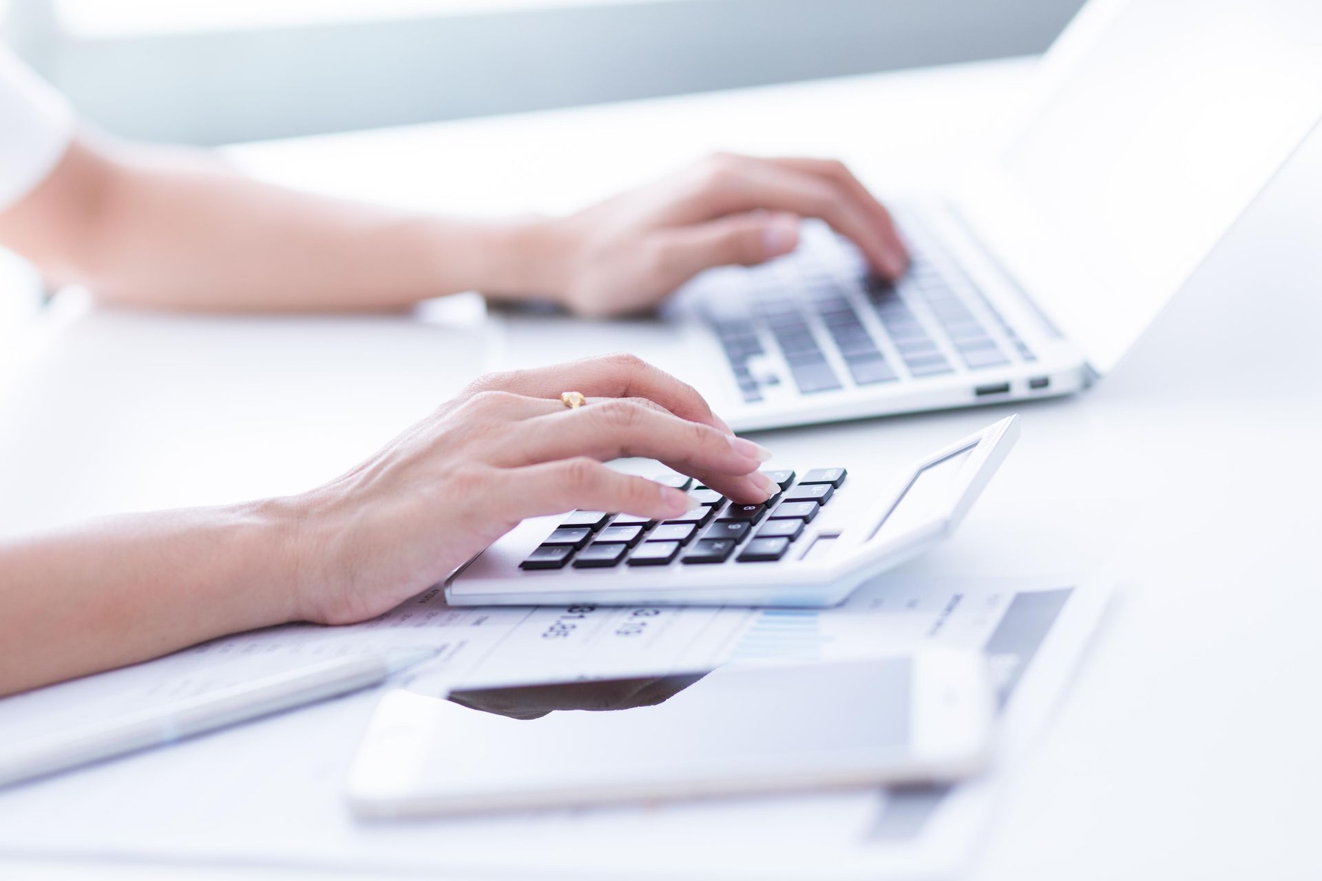 A person is typing on a laptop and using a calculator.
