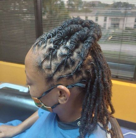 Woman with black locs, some in a half-up style, wearing a mask in a salon setting.