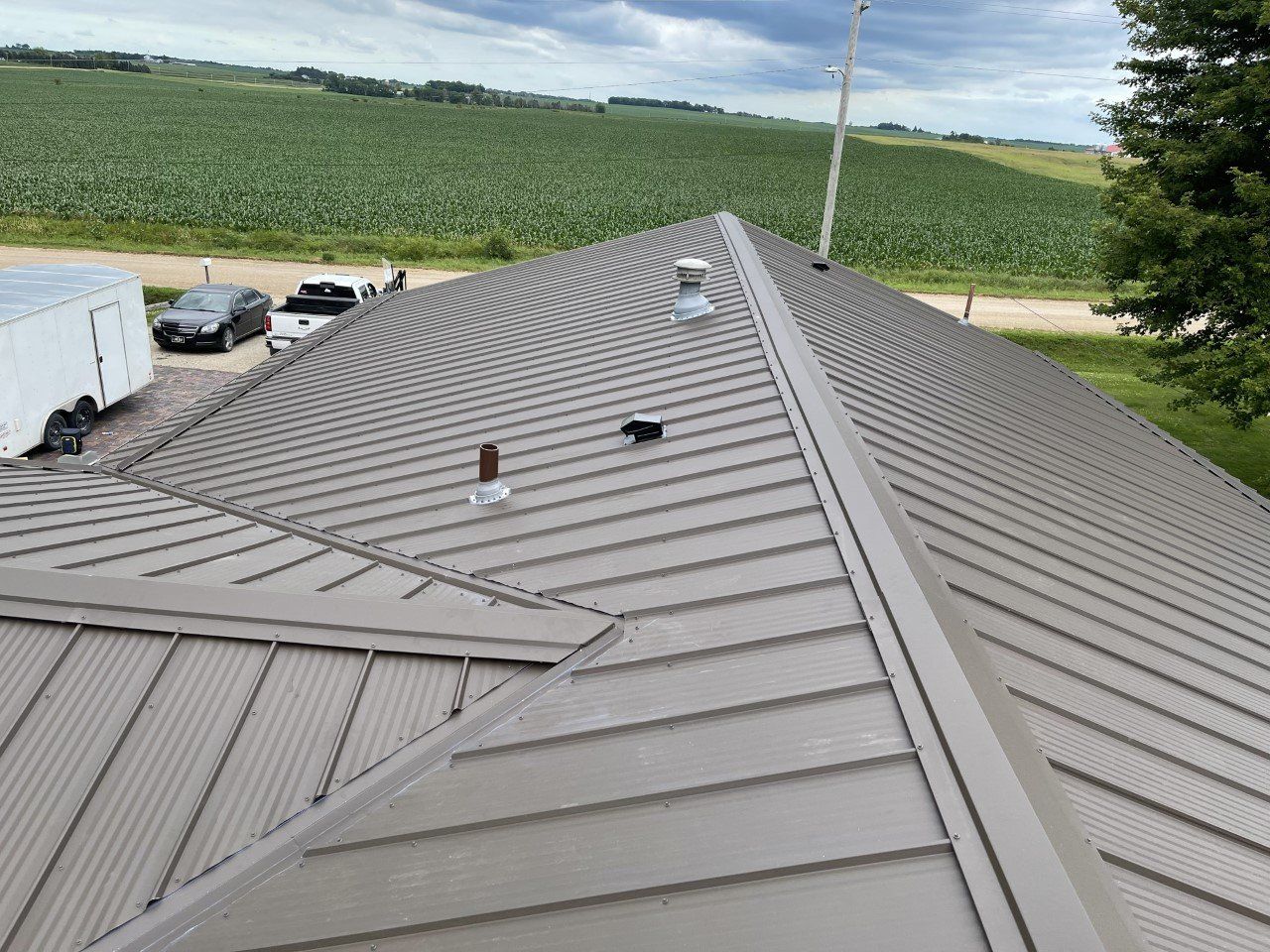 Brown metal roof on a building, with vents and a backdrop of farmland.