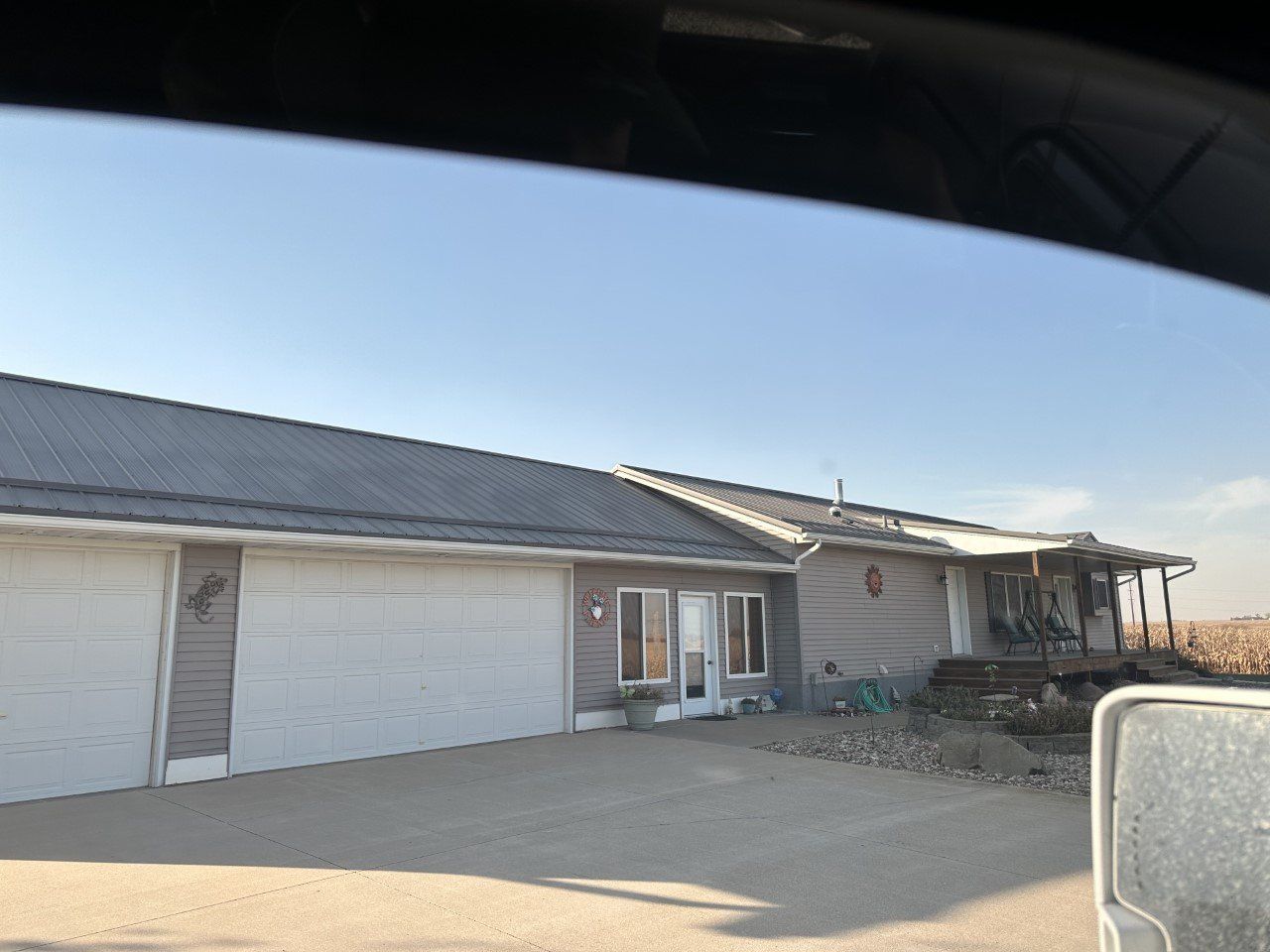 A gray house with a metal roof, a garage with two doors, and a porch under a clear blue sky.