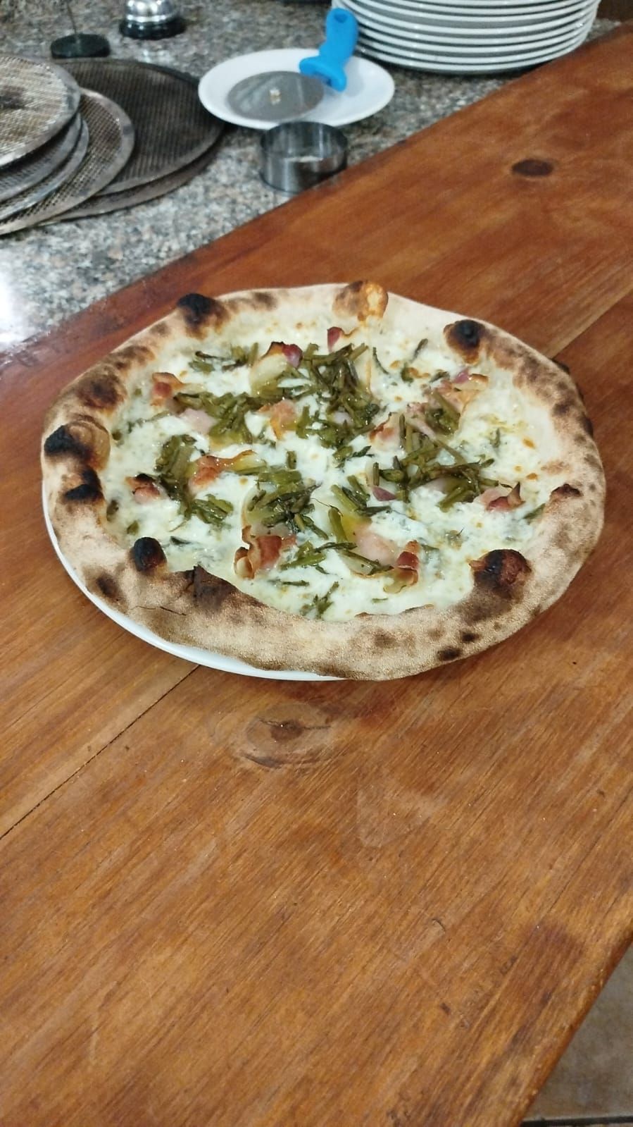 Una piccola pizza su un tavolo di legno in un ristorante, condita con formaggio ed erbe aromatiche.