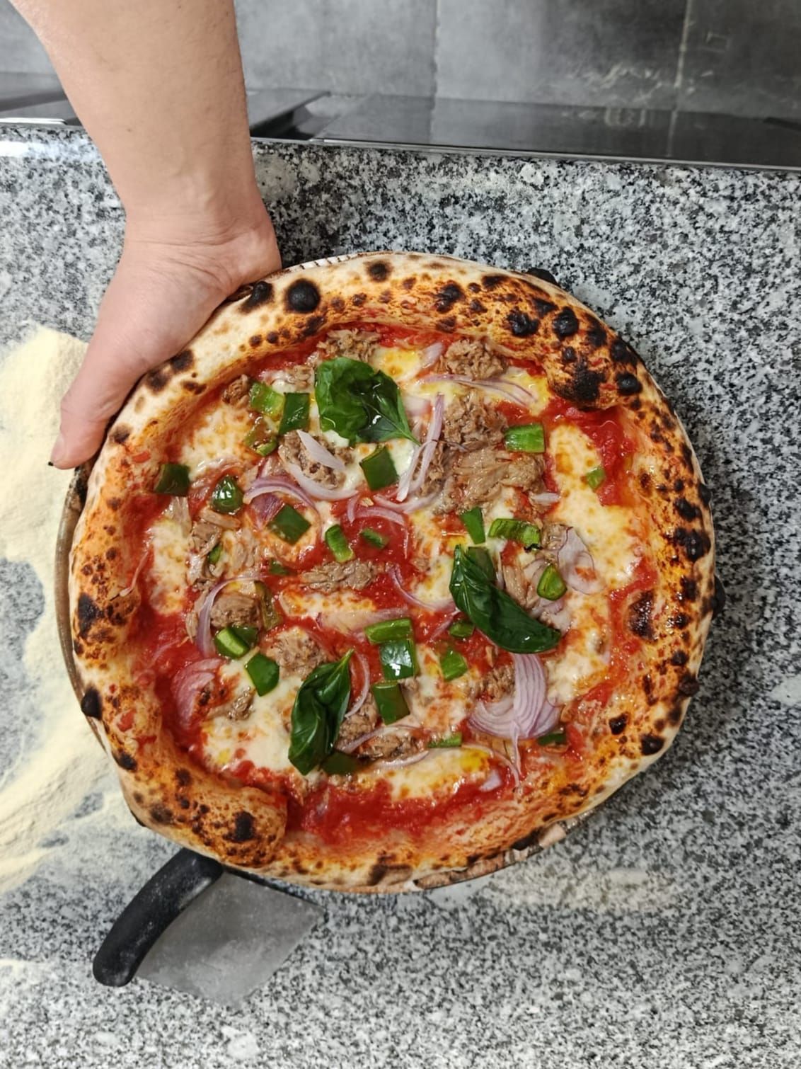 Una mano che regge una pizza margherita appena sfornata su un piano di lavoro in granito.