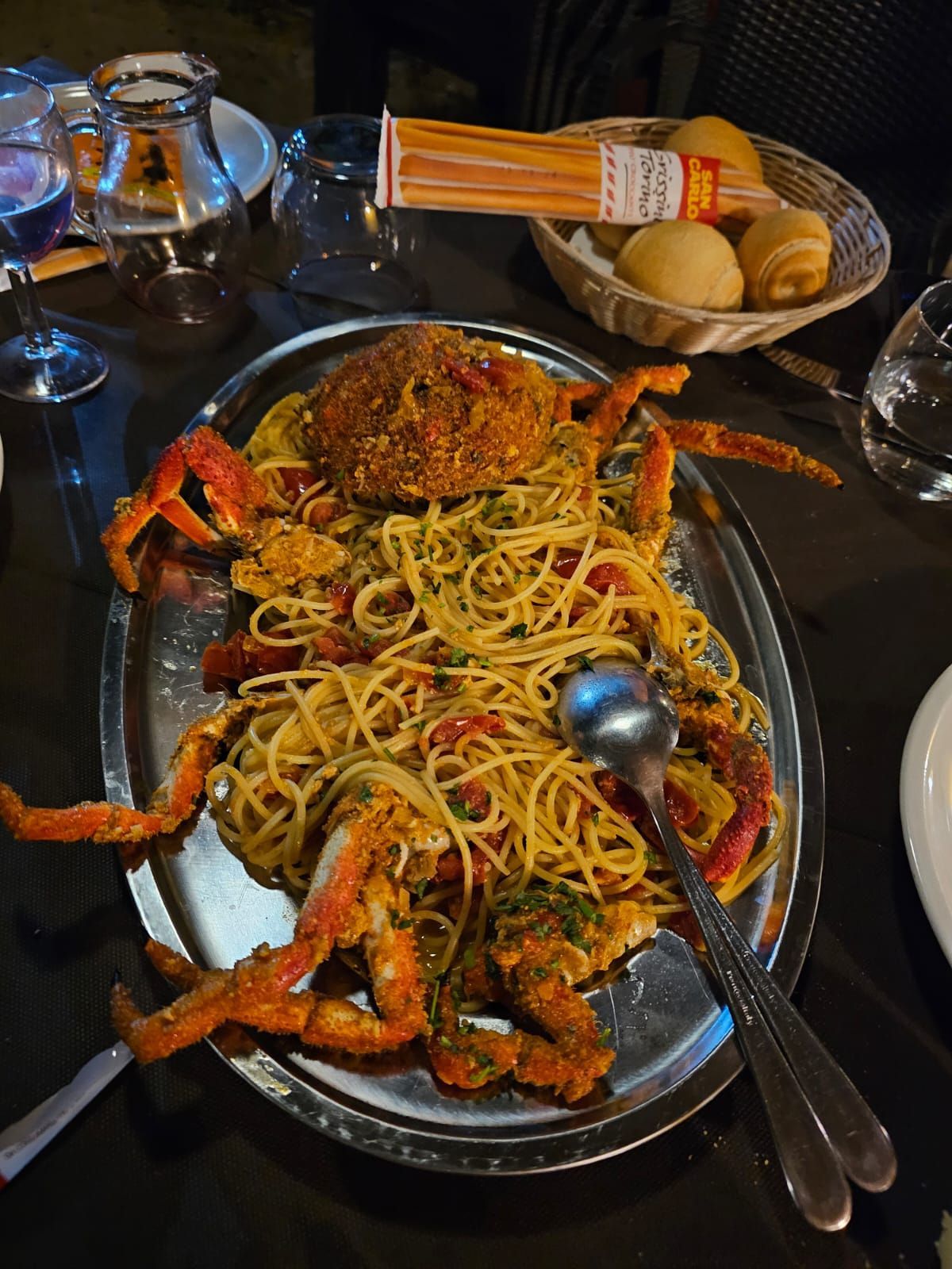 Piatto di pasta ai frutti di mare con granchi su un tavolo scuro, accanto a pane e teiera.