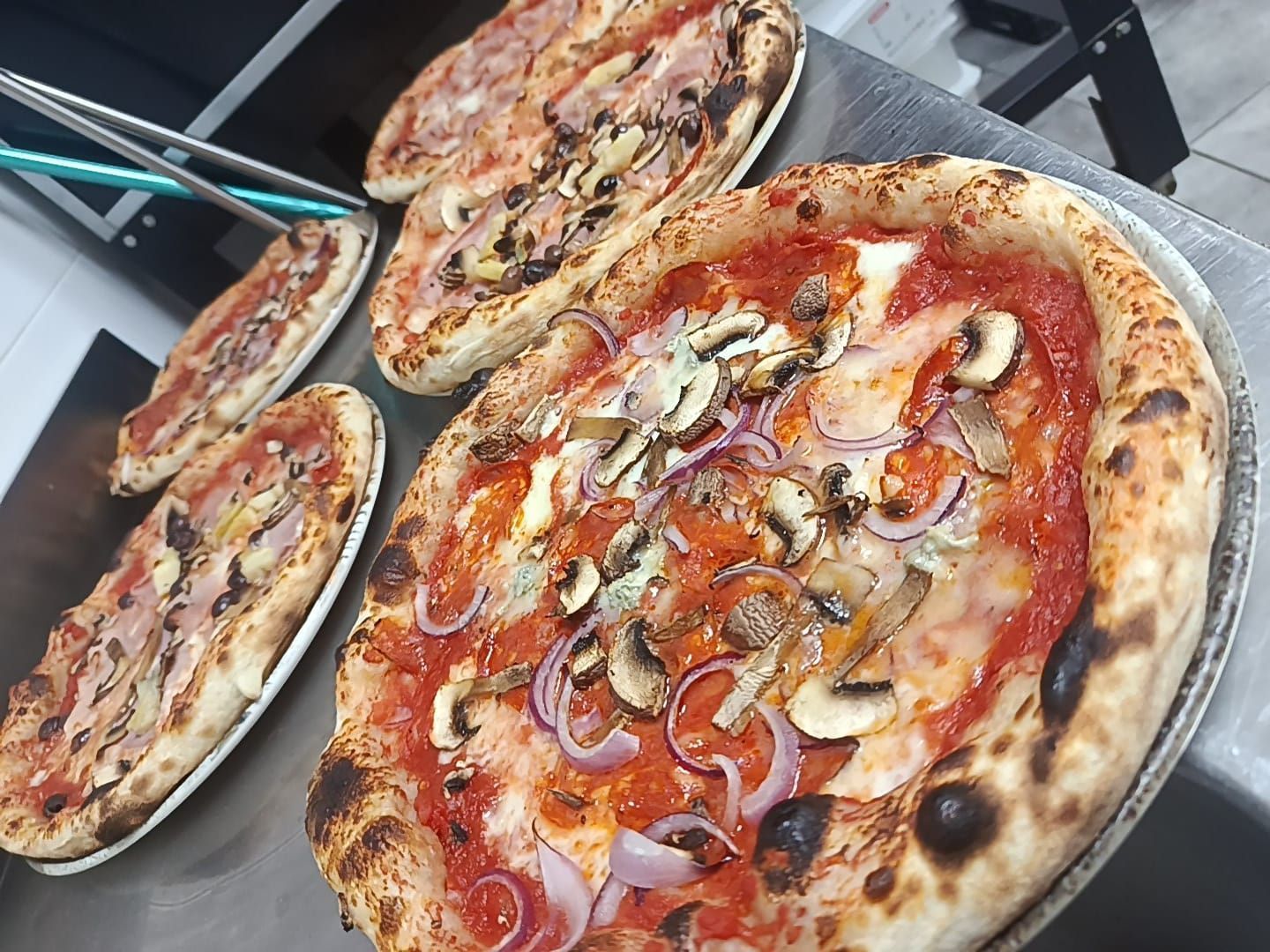 Tre pizze appena sfornate con vari condimenti su vassoi, viste dall'alto su un tavolo