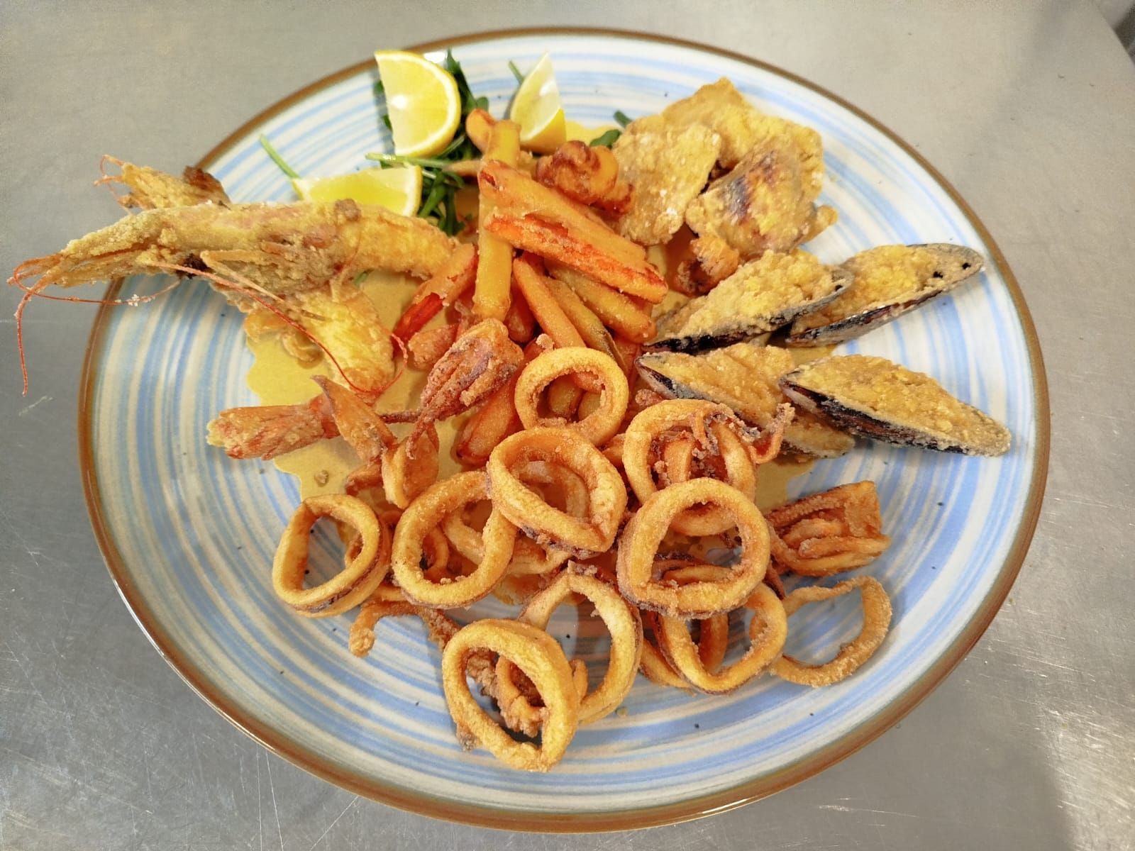 Piatto di frutti di mare fritti misti con anelli di calamari, gamberi e spicchi di limone su un piatto a righe.