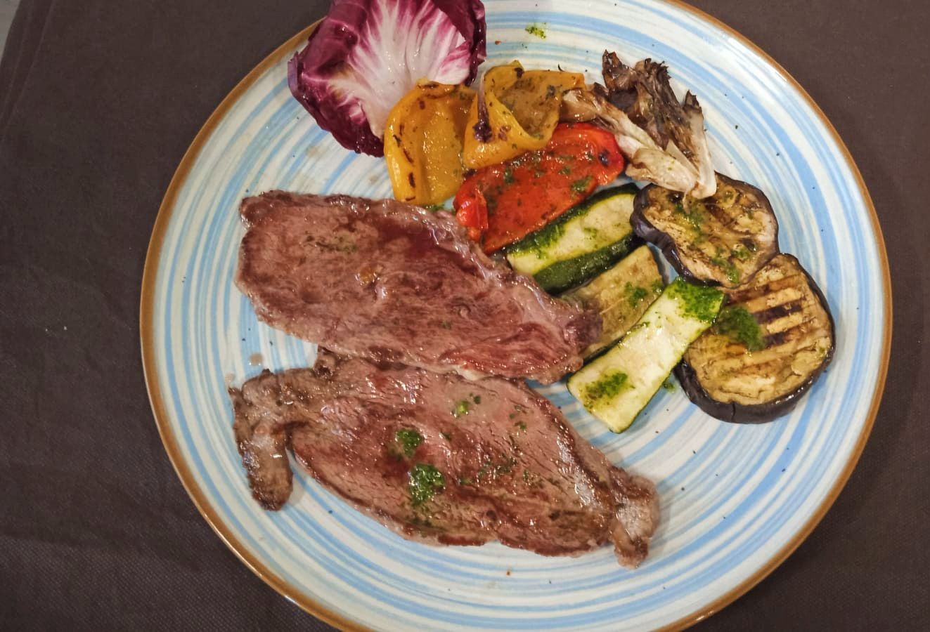 Bistecca alla griglia con verdure arrosto e radicchio su un piatto dal bordo blu.