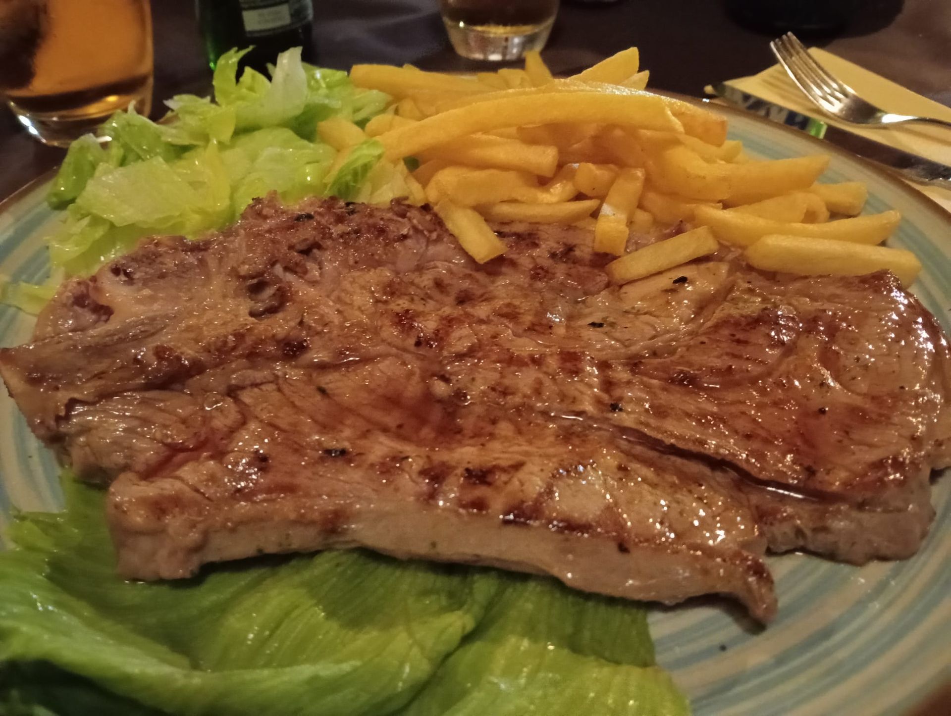 Bistecca alla griglia con patatine fritte e lattuga su un piatto a un tavolo di ristorante.