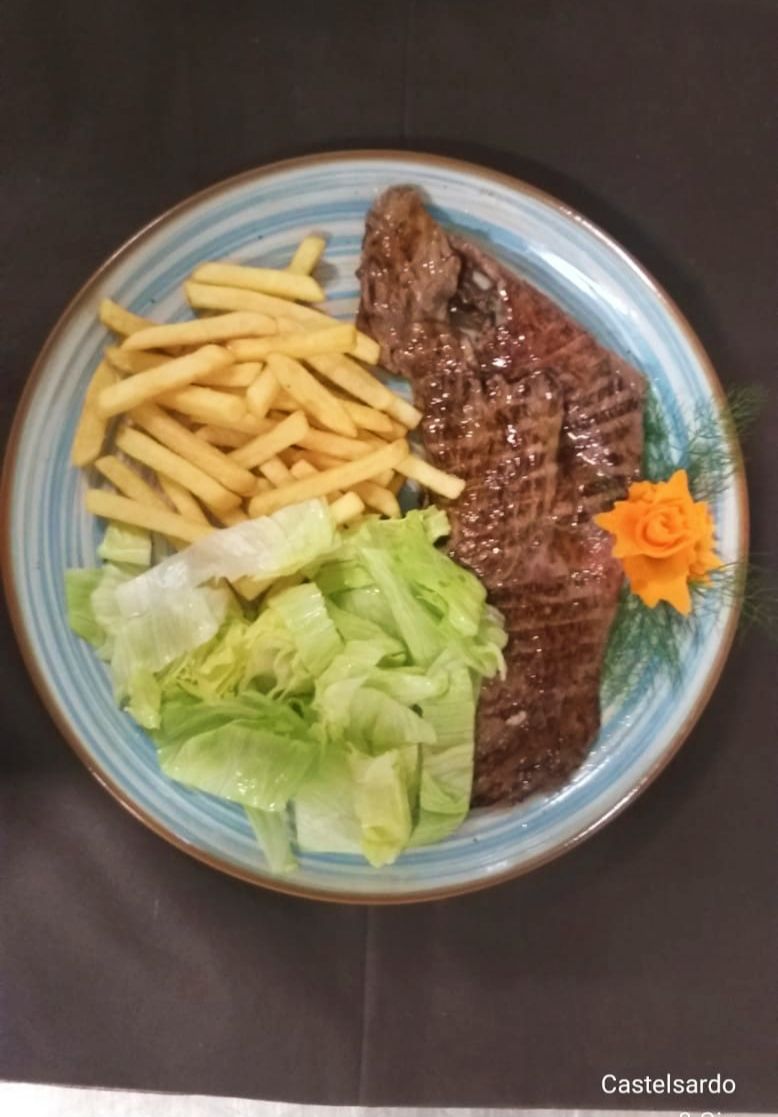 Piatto con carne grigliata, patatine fritte, lattuga e guarnizione di carote su un tavolo scuro.