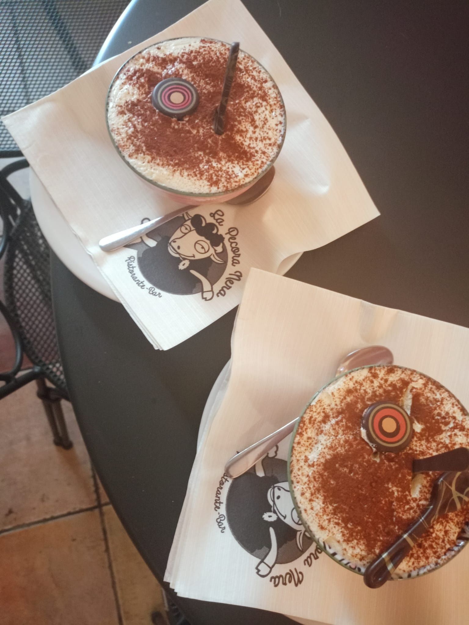 Due bevande al caffè schiumose con cannella su vassoi neri su un tavolino da bar.
