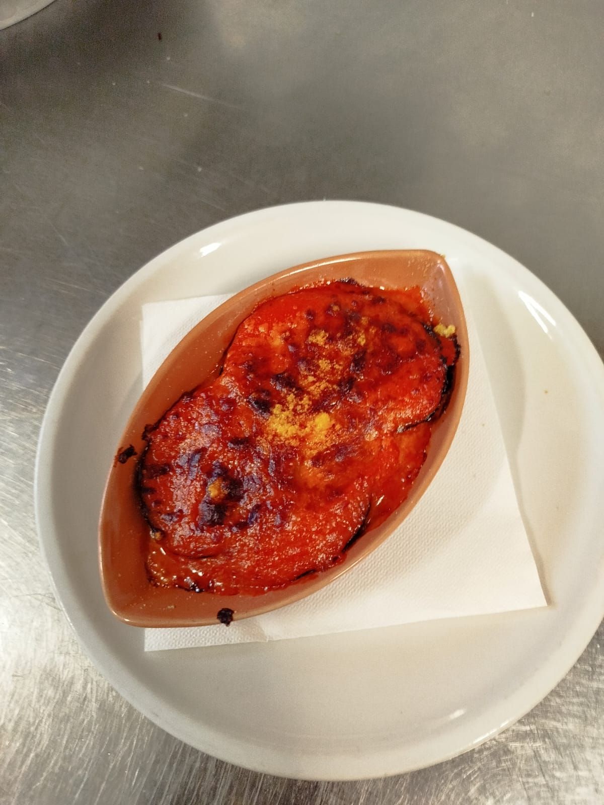 Un piccolo dolce al forno servito in una pirofila a forma di barchetta su un piatto bianco, guarnito con frutta caramellata o glassa.