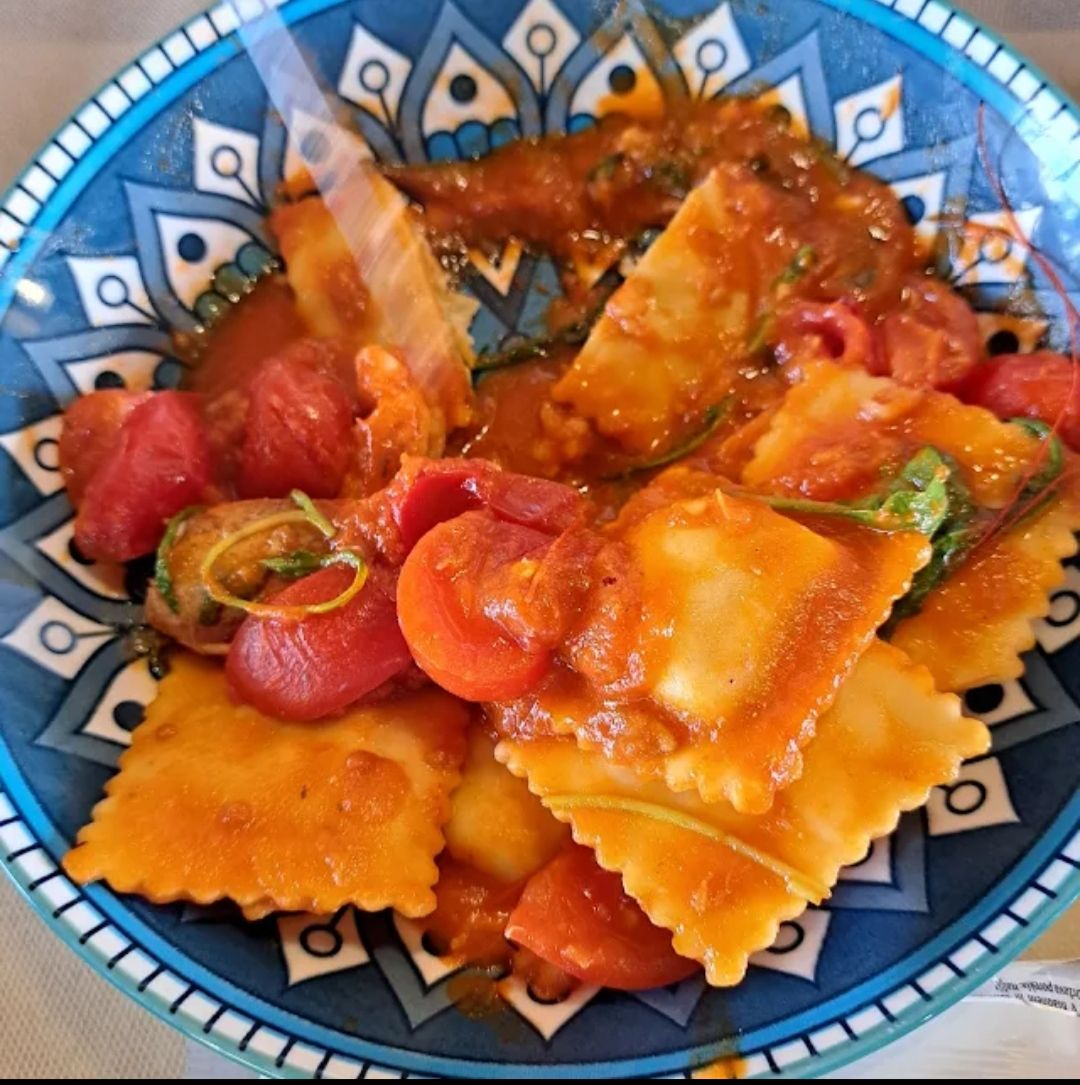 Ravioli colorati in salsa di pomodoro su un piatto decorato di blu.