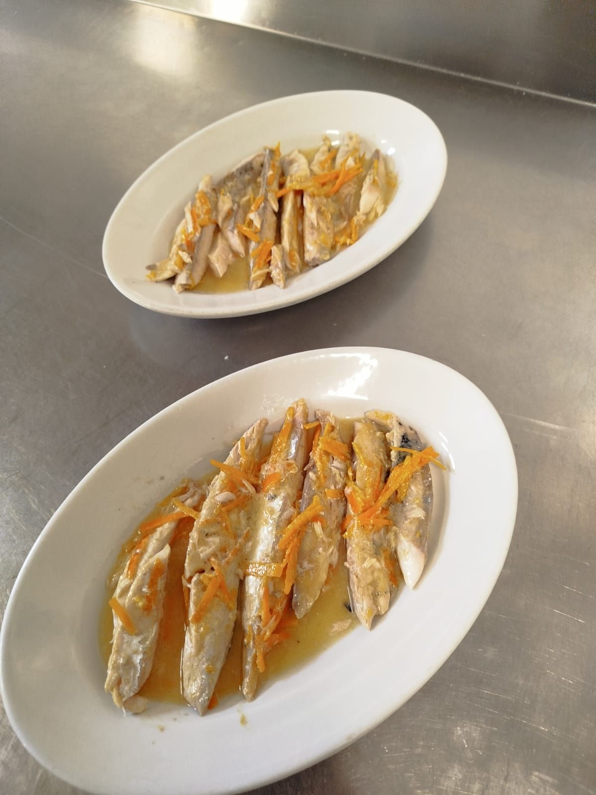 Due piatti di pesce cotto a fette, conditi con salsa, su un tavolo in acciaio inox.
