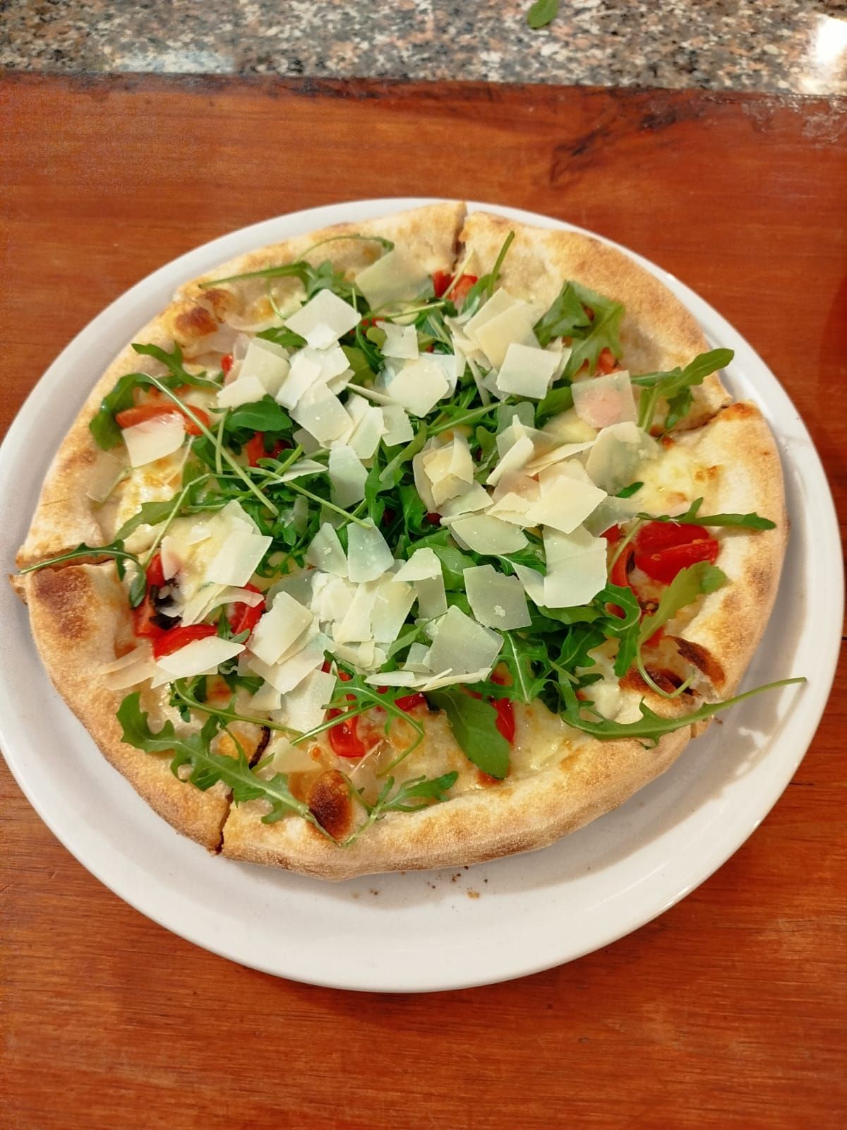 Pizza bianca con rucola e formaggio grattugiato su un piatto appoggiato su un tavolo di legno.