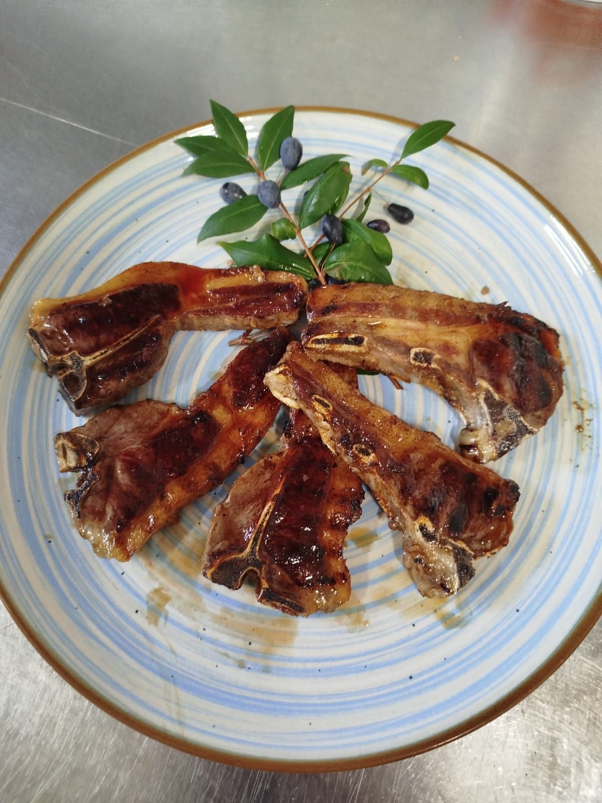 Cinque strisce di carne grigliata glassate, disposte su un piatto bianco e guarnite con erbe aromatiche.
