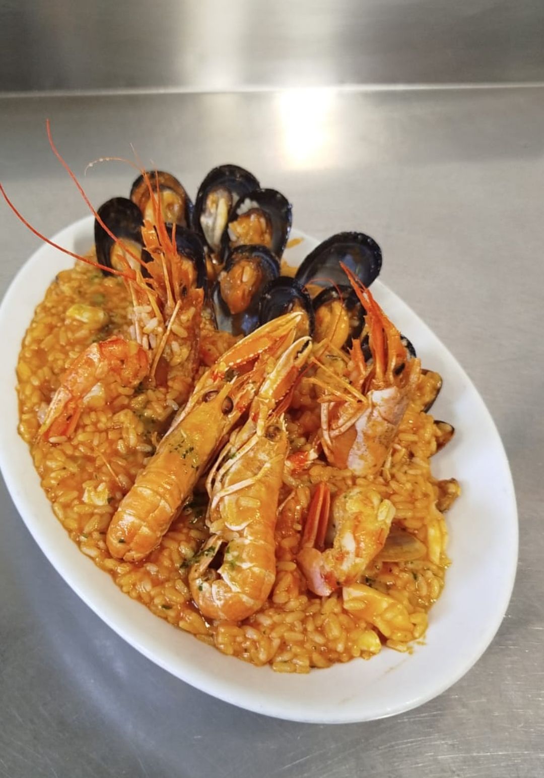 Piatto di pesce con riso e cozze su un piatto bianco in un ambiente di cucina.