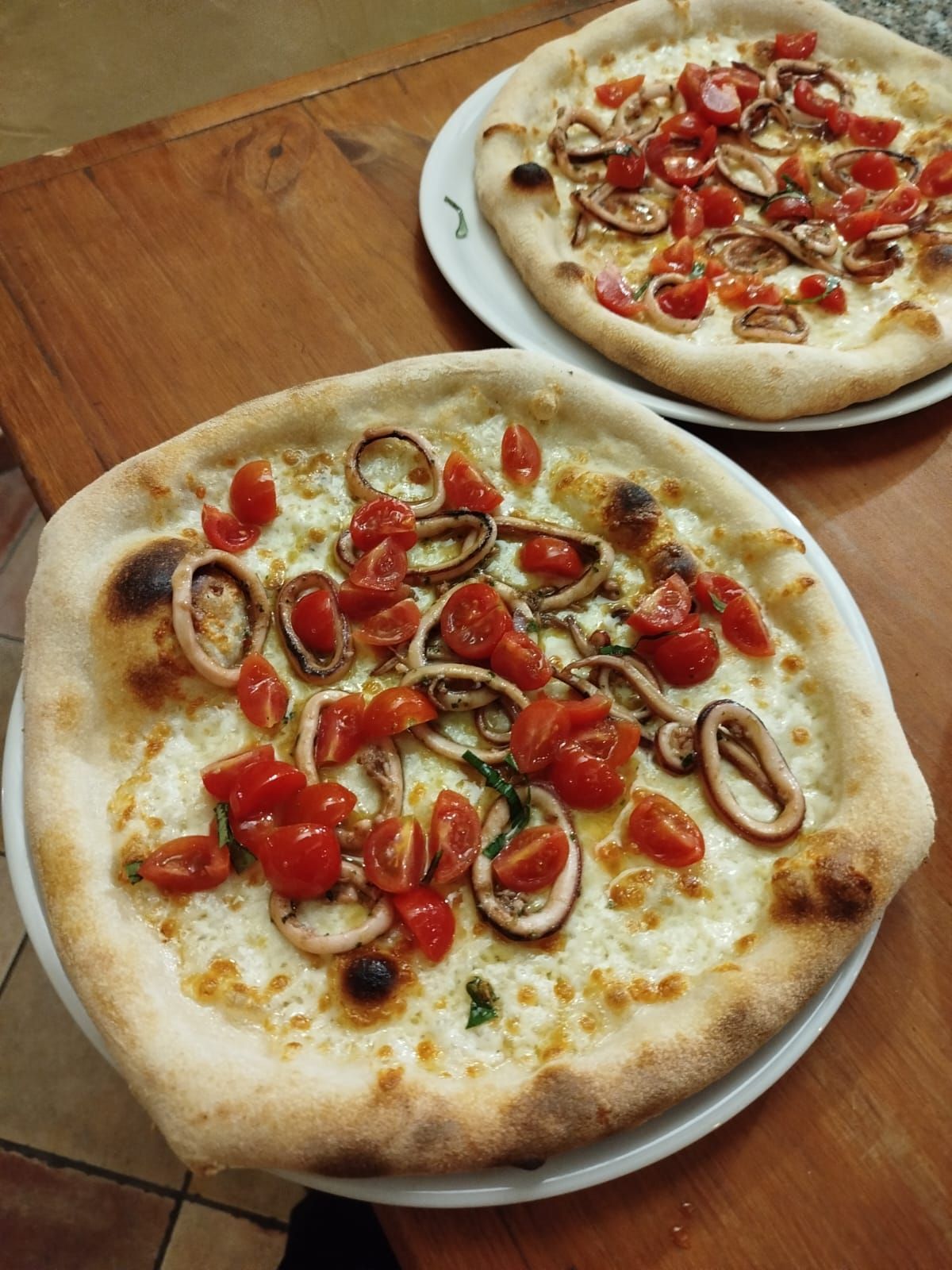 Due piccole pizze con pomodorini e anelli di calamari su un tavolo di legno.