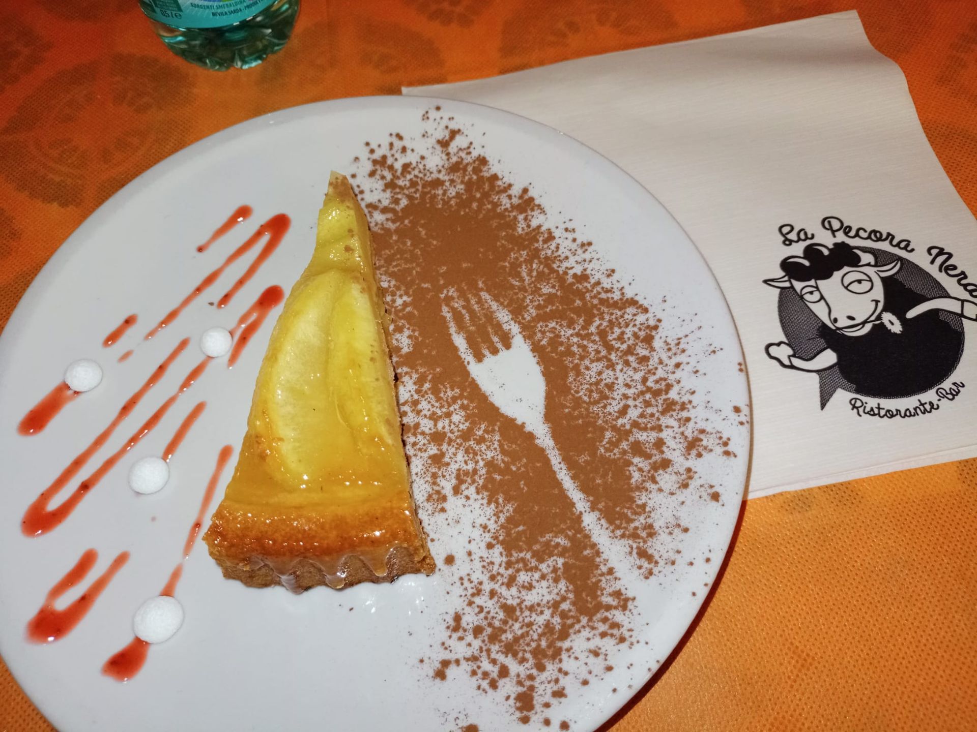 Piatto da dessert con una fetta di torta, spolverata di cioccolato e decorazioni di salsa bianca e rossa su un tavolo