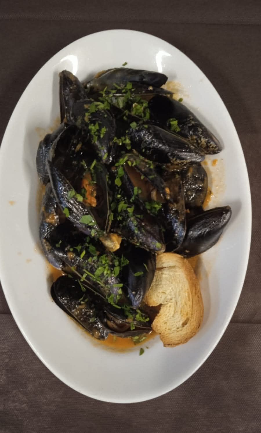 Piatto di cozze nere in salsa alle erbe con una fetta di pane su un piatto bianco.