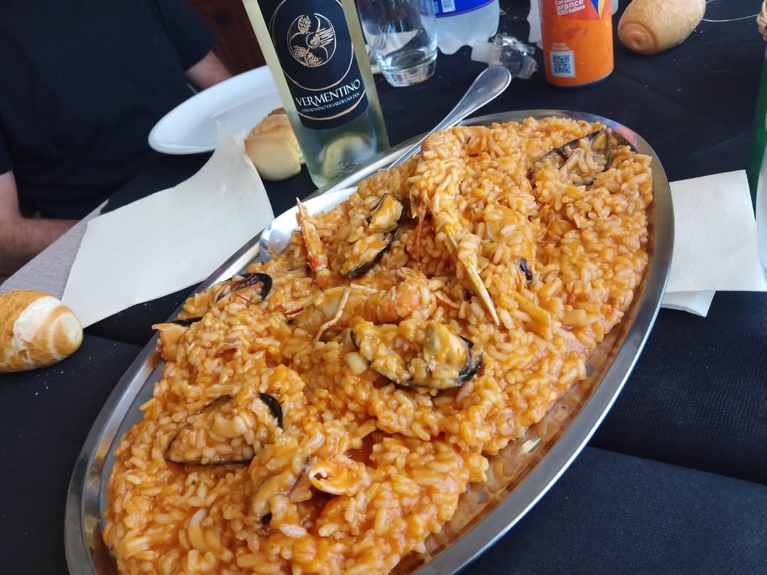 Su un tavolo di ristorante, un vassoio ovale con riso all'arancia e frutti di mare, con una bottiglia e del pane nelle vicinanze.