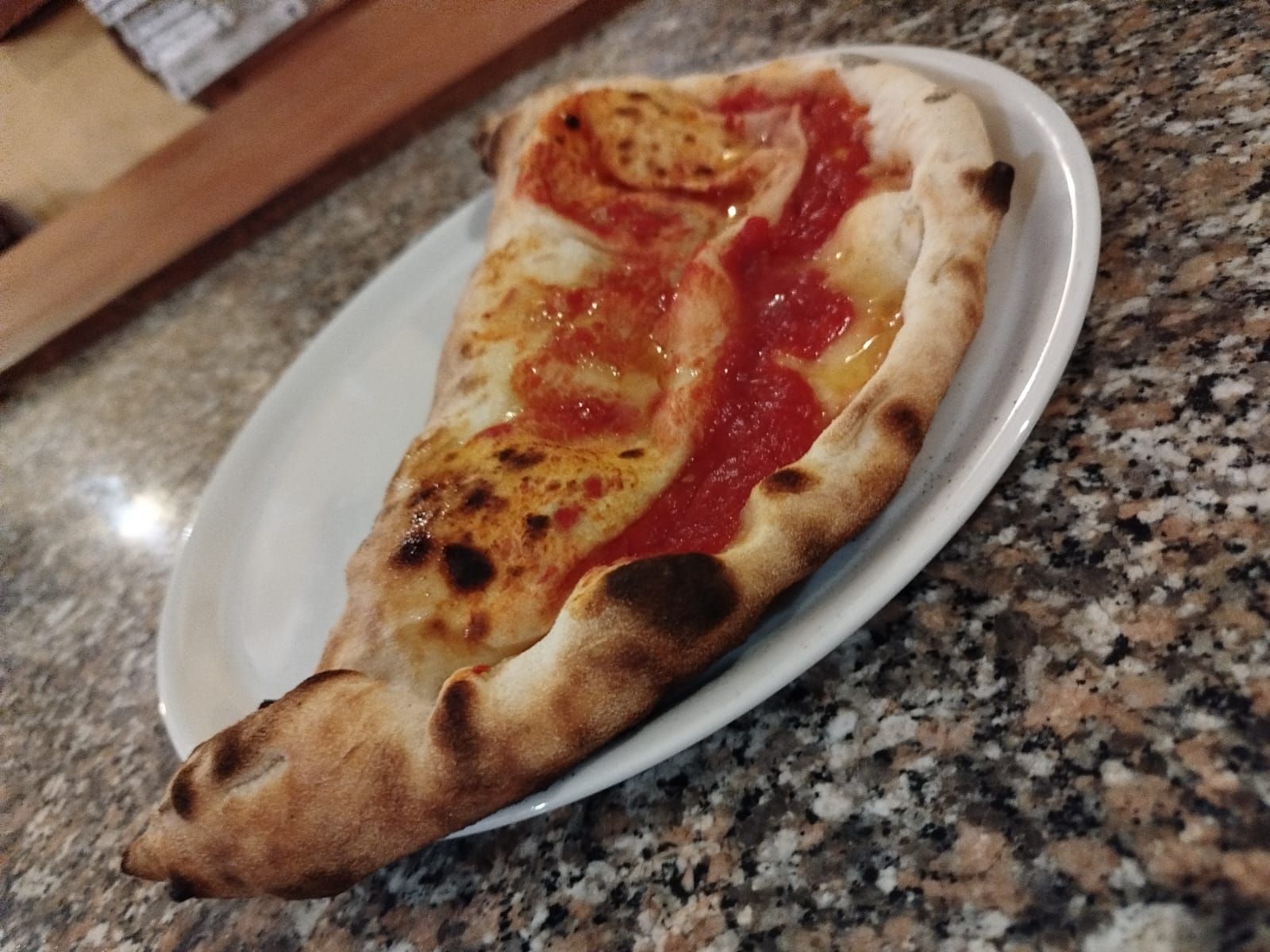 Una fetta di pizza margherita su un piatto bianco appoggiato su un piano di lavoro in granito screziato.