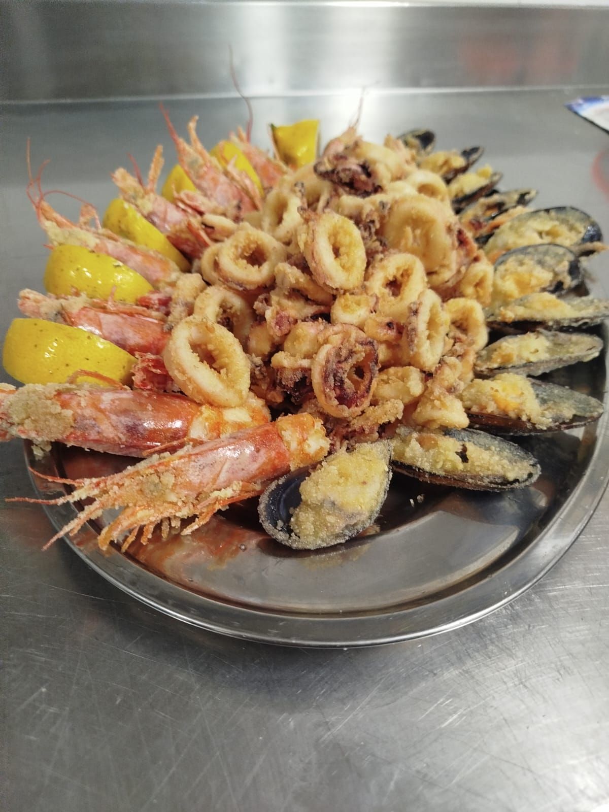 Piatto di frutti di mare con gamberi, anelli di calamari, cozze e spicchi di limone su un vassoio di metallo.