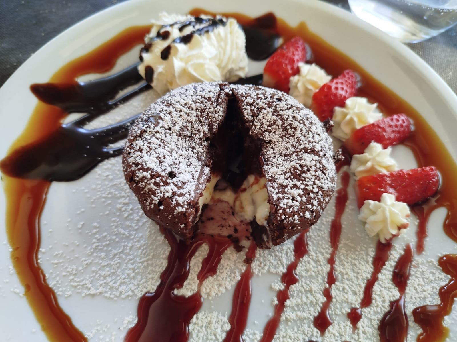 Piatto da dessert con torta al cioccolato in polvere, panna montata, fragole e salsa al cioccolato.