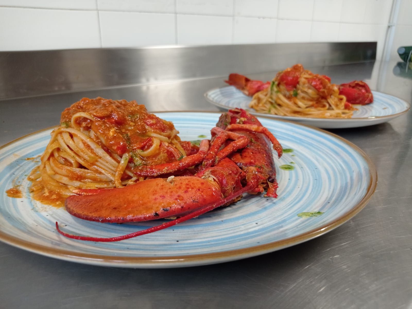 Piatti di pasta all'astice su un bancone, con code di aragosta rossa e spaghetti in un ambiente di cucina.