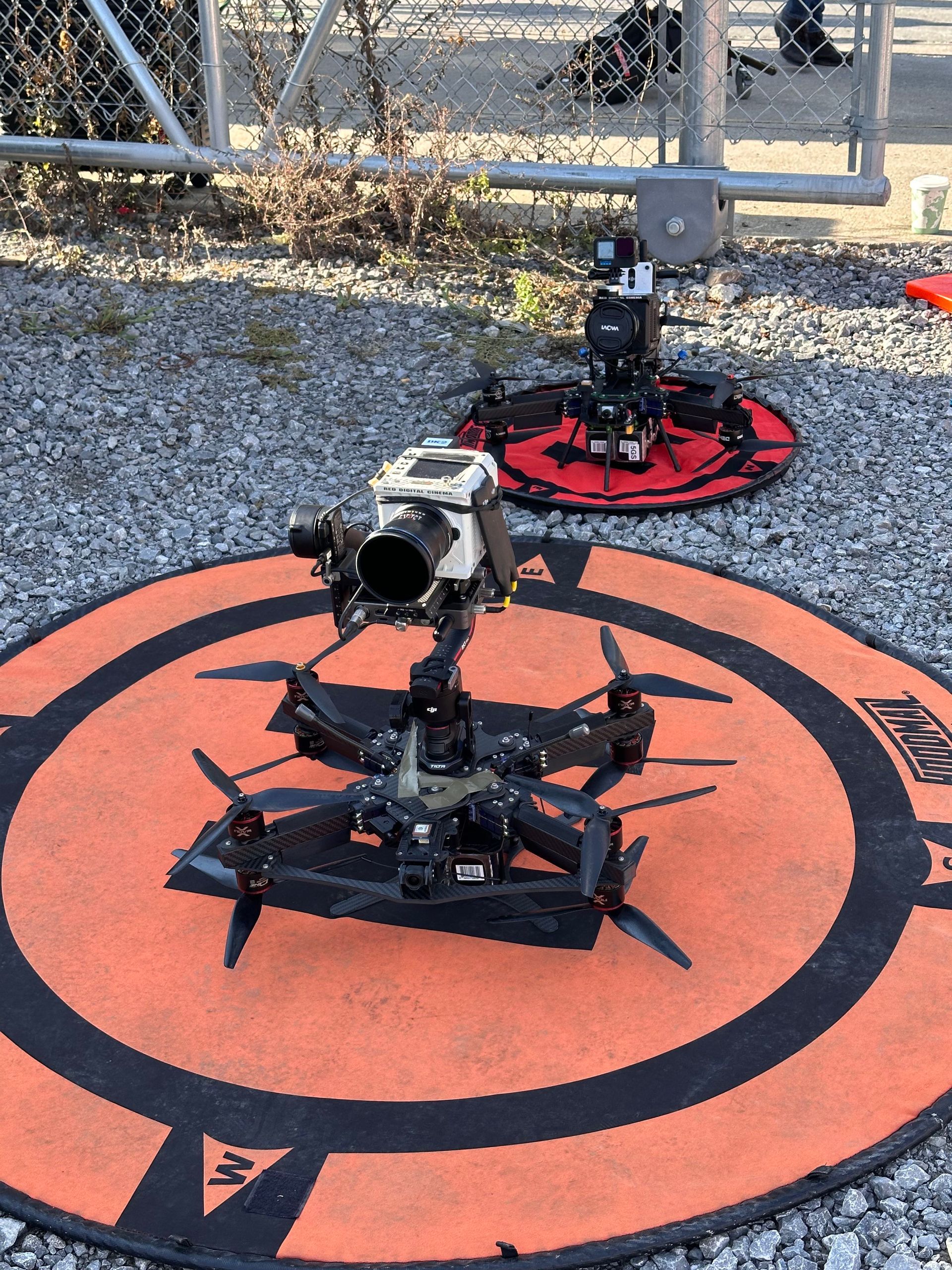 Two drones are sitting on top of an orange mat with the letter m on it