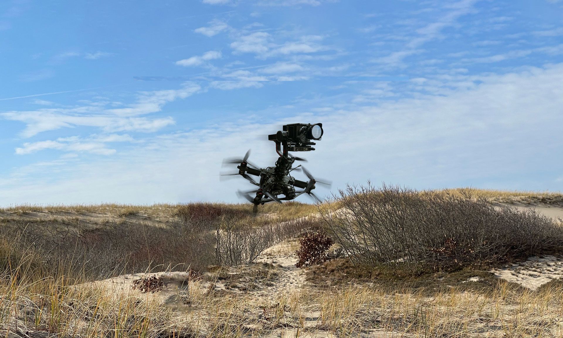 A drone is flying over a dry grass field.