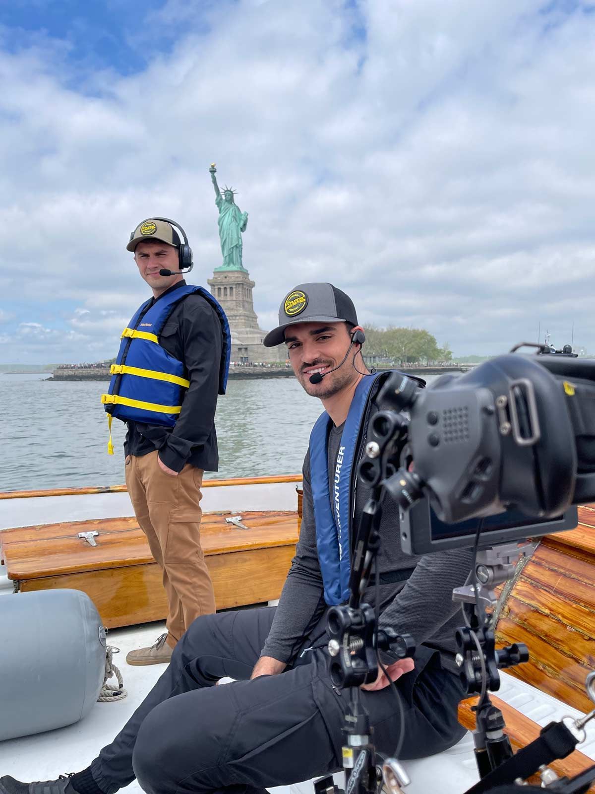 A man sitting on a boat with a camera in front of a statue of liberty