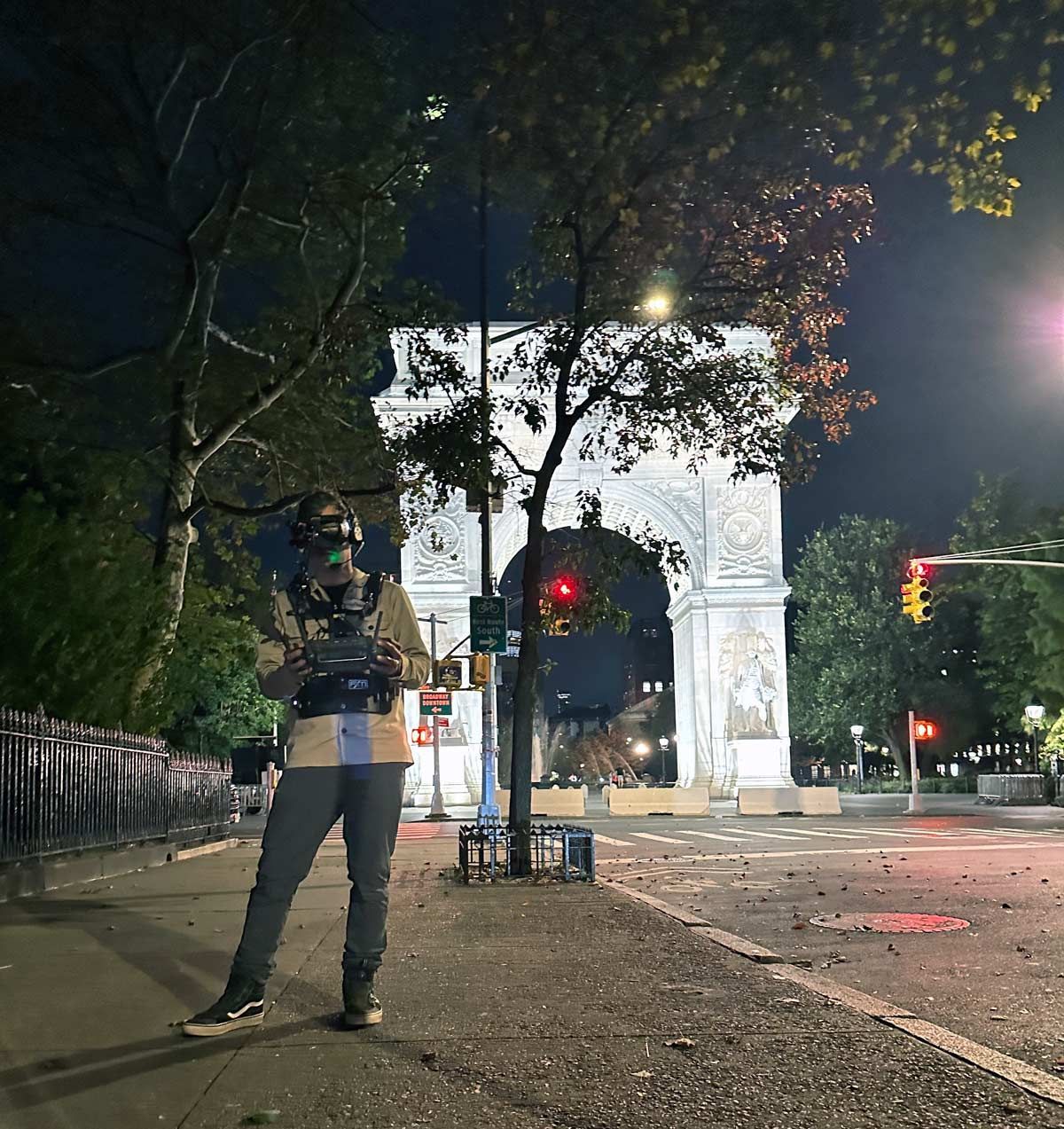 A man is standing on a sidewalk in front of a large archway at night