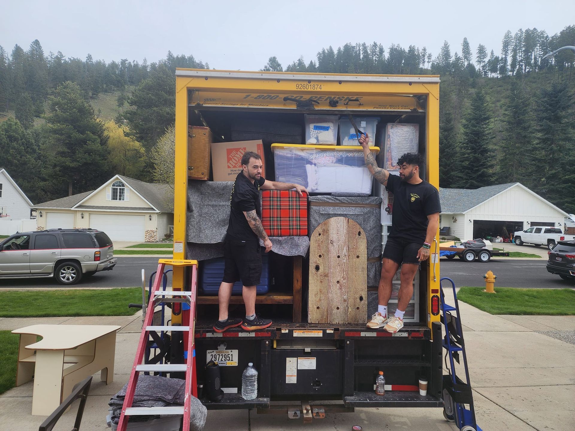 Two men are standing on the back of a moving truck.