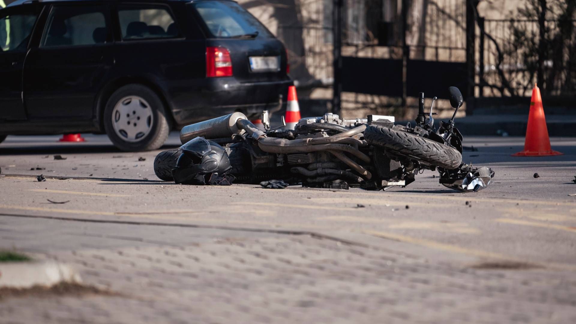 A motorcycle has crashed into a car on the side of the road.