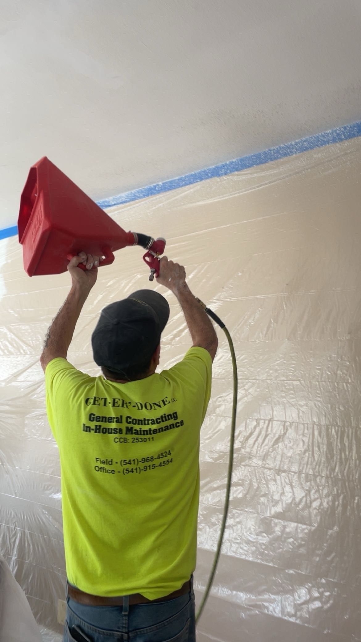 Painter in red cap and shirt spray-painting a ceiling with a spray gun. Painter in red cap and shirt spray-painting a ceiling with a spray gun.