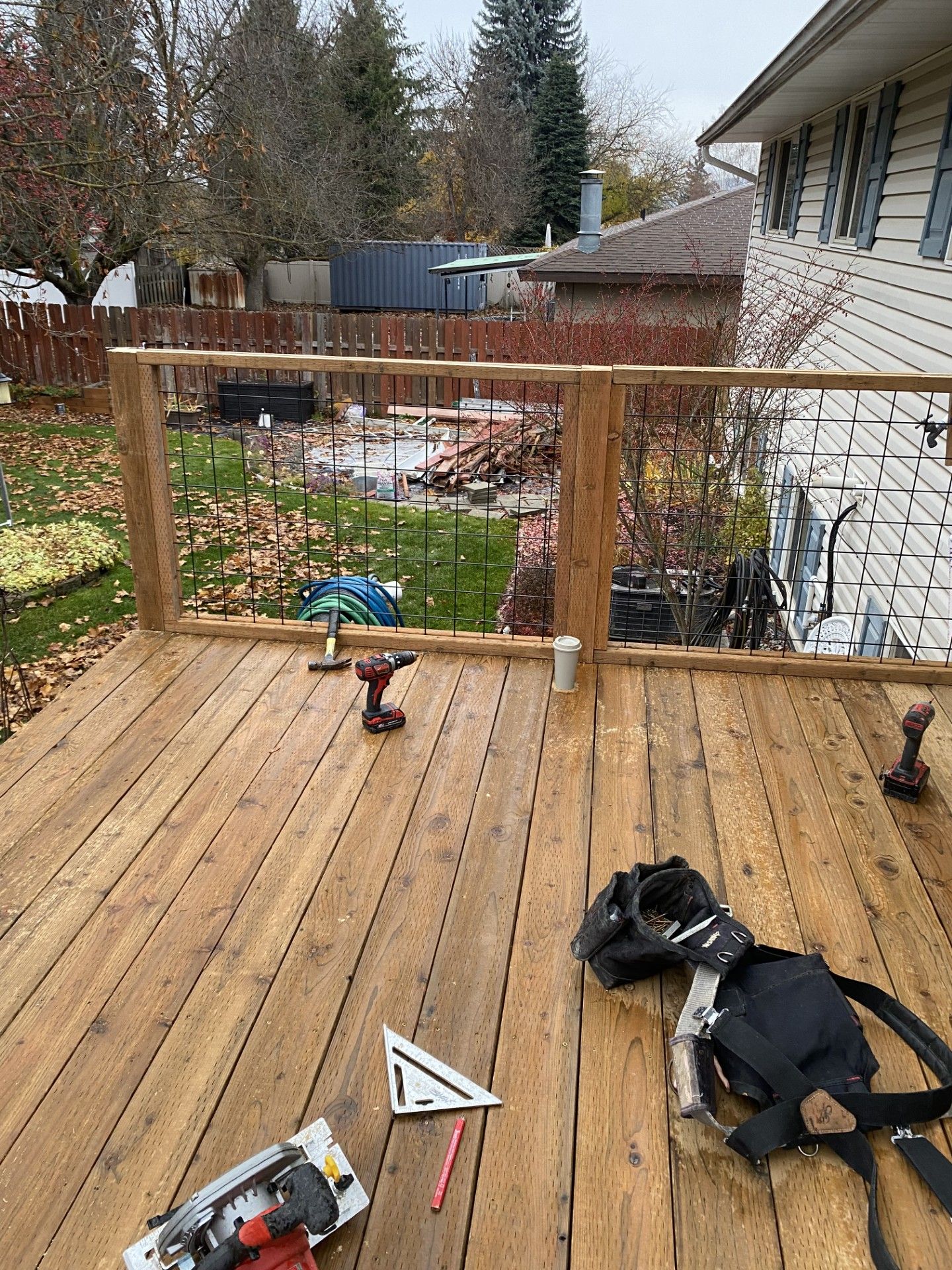 Wooden deck beside a gray house, with white railing and trees in the background. Wooden deck beside a gray house, with white railing and trees in the background.