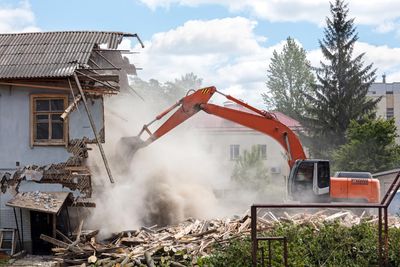 Excavator demolishing a house, kicking up dust at a construction site.