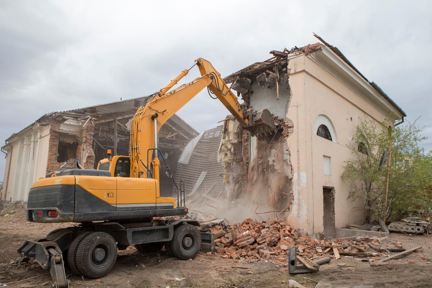 Yellow excavator demolishing a damaged building, with rubble falling around the site Yellow excavator demolishing a damaged building, with rubble falling around the site