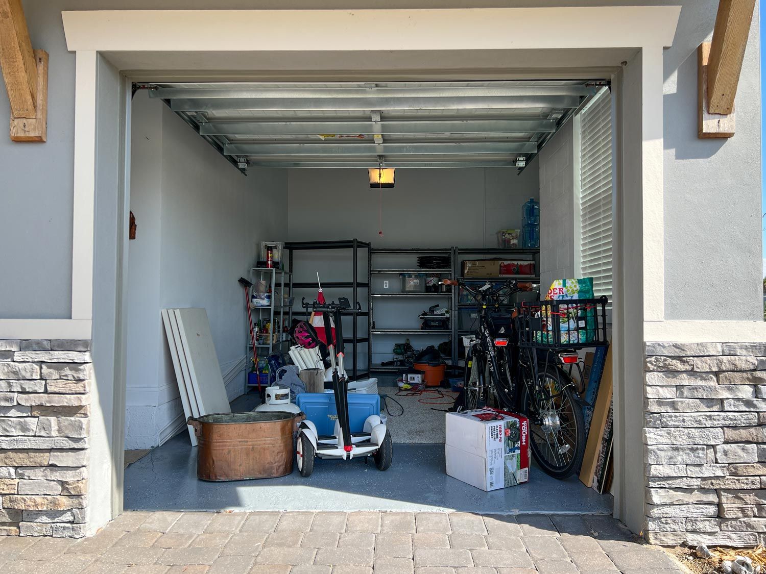 Open garage with shelves, bins, bikes, and a child’s scooter inside. Open garage with shelves, bins, bikes, and a child’s scooter inside.