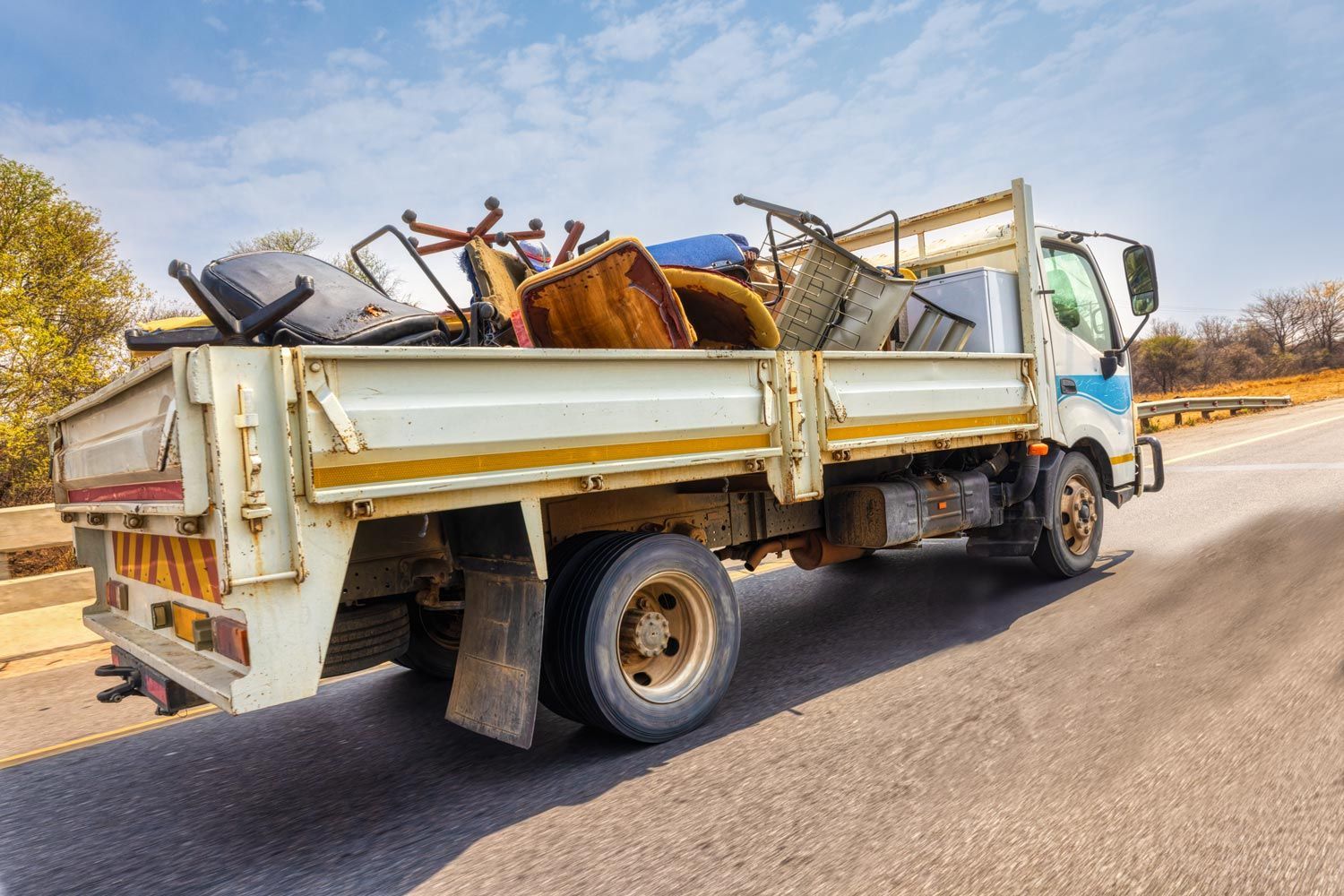 White flatbed truck hauling scrap metal on a roadside in bright daylight White flatbed truck hauling scrap metal on a roadside in bright daylight