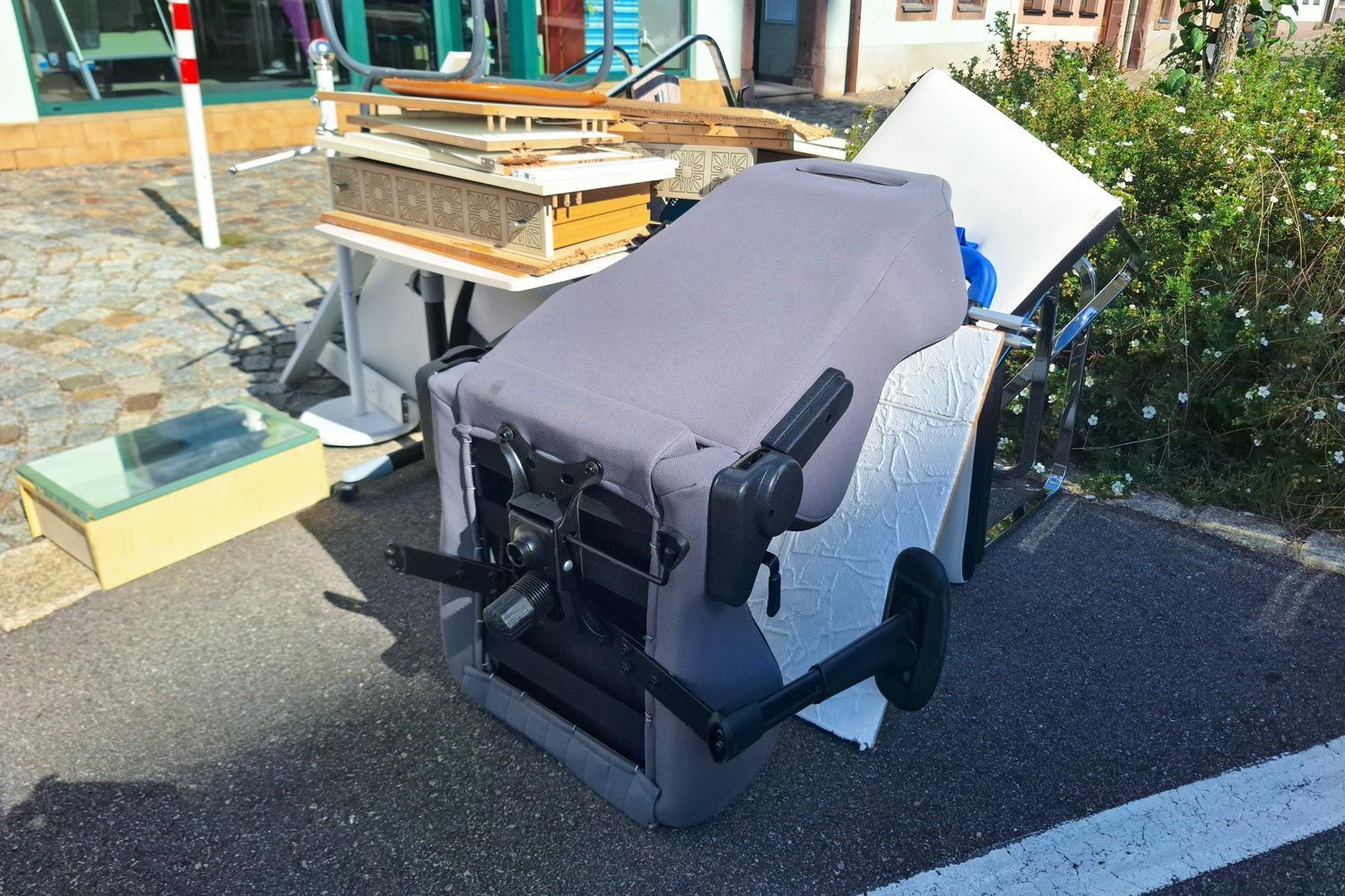 Wheelchair with a gray cover parked outdoors beside a curb and bushes, with furniture in the background Wheelchair with a gray cover parked outdoors beside a curb and bushes, with furniture in the background