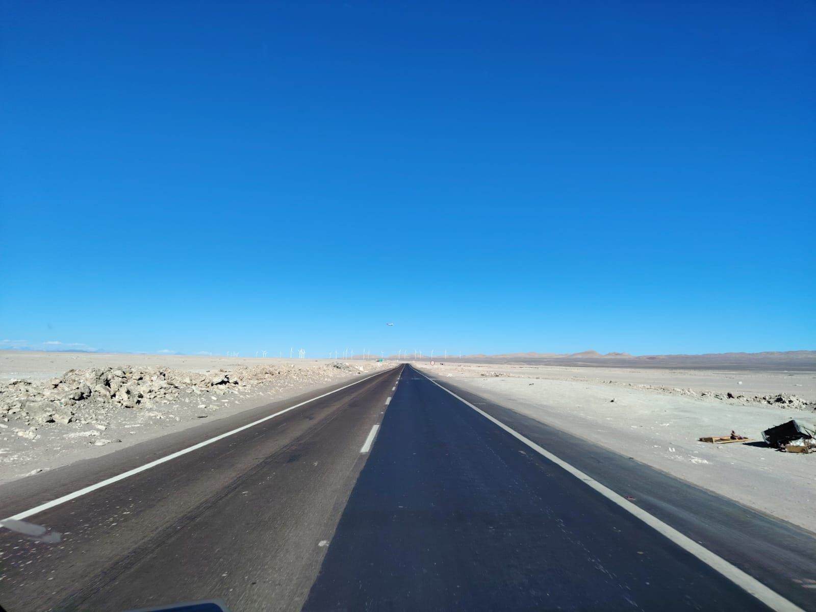 Una carretera recta de asfalto se extiende hacia un vasto y árido paisaje desértico bajo un cielo azul claro y brillante.