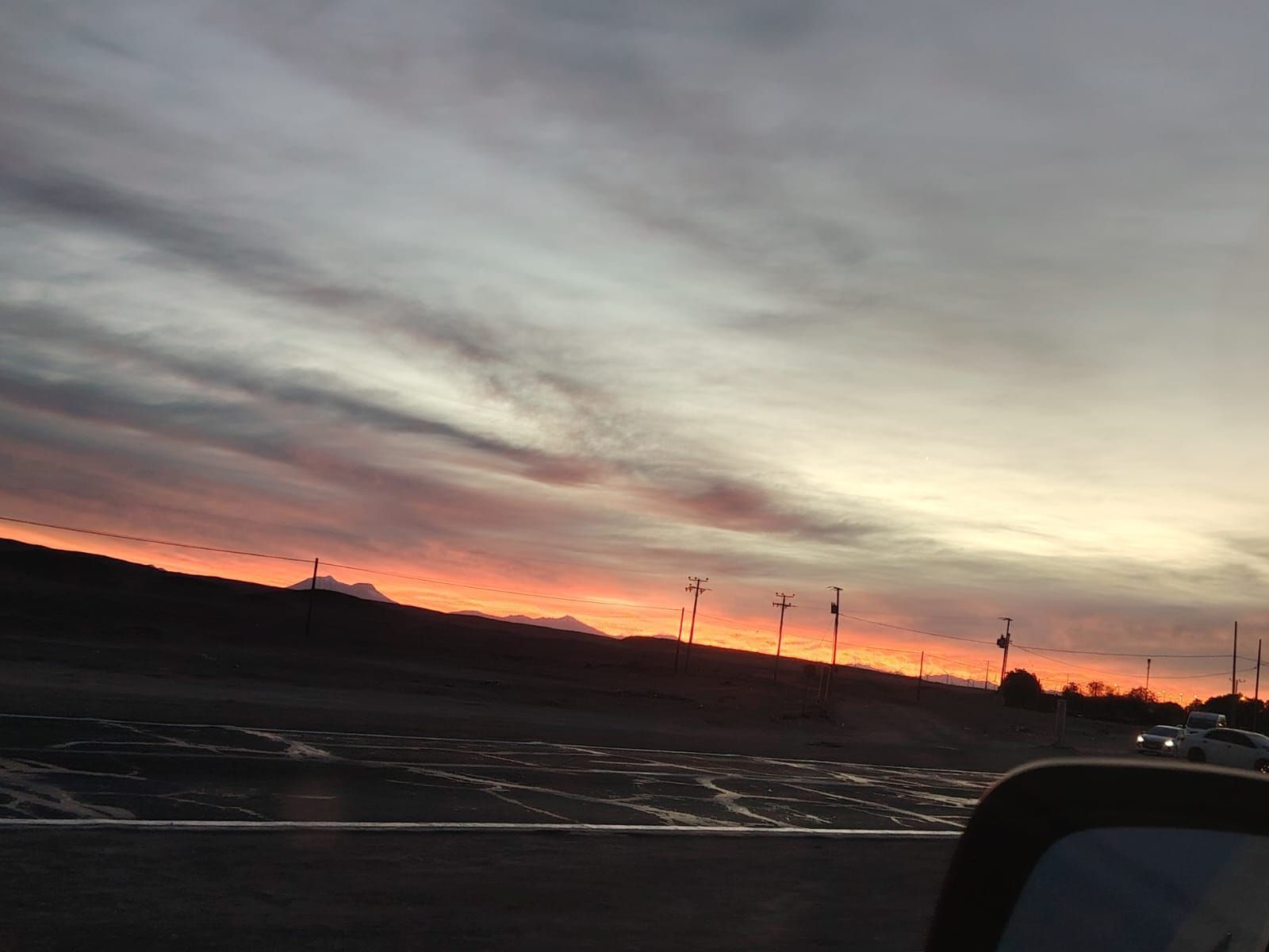 Una vibrante puesta de sol con vetas de nubes naranjas, rosas y grises sobre un paisaje