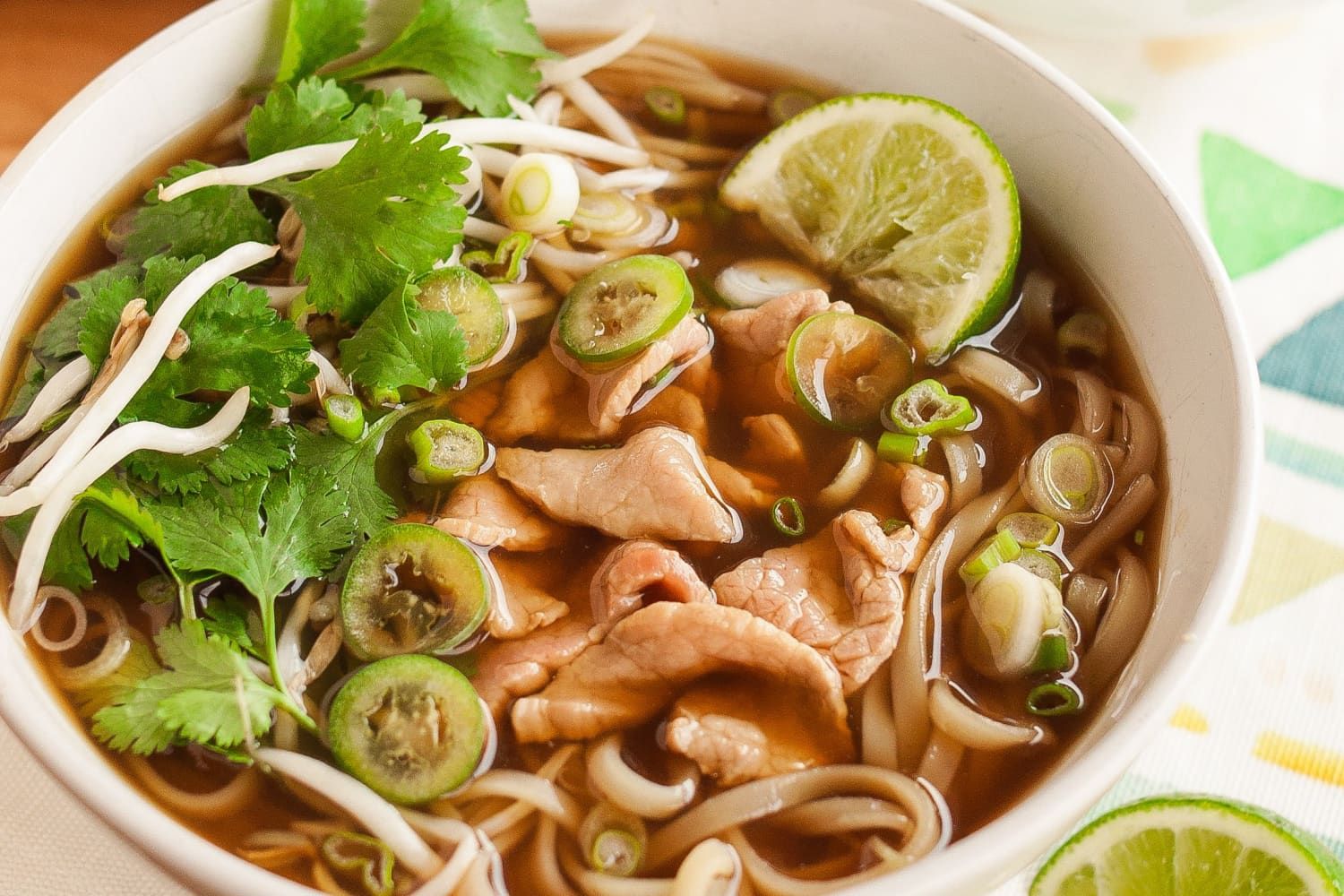 Bowl of pho with noodles, meat, bean sprouts, cilantro, green onions, and lime.
