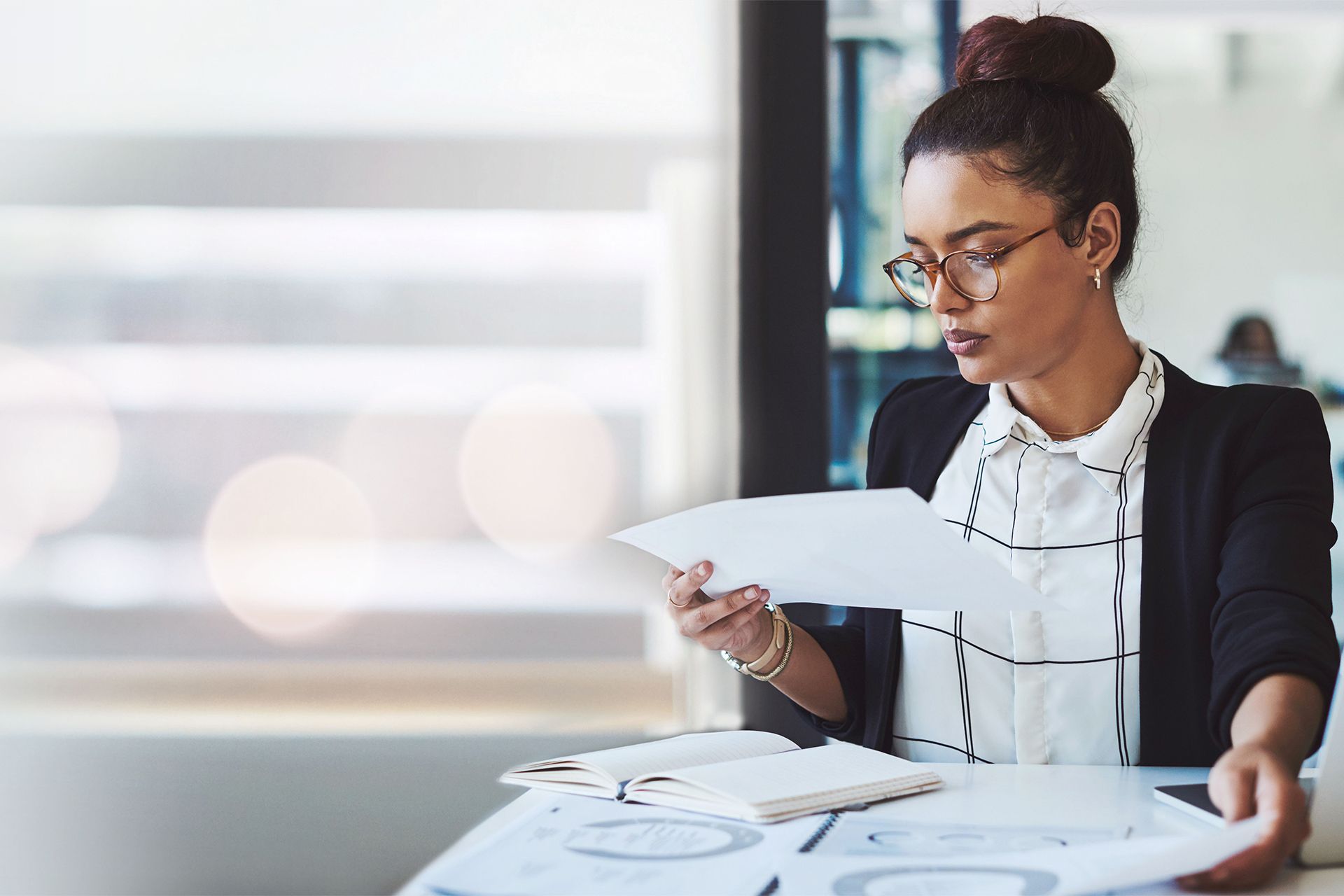Woman in glasses reviewing papers at a desk in a bright office