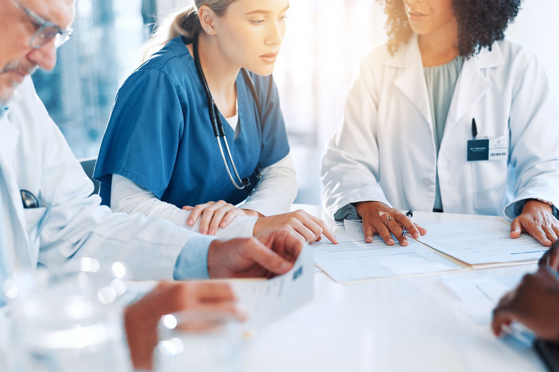 Medical team in white and blue coats discussing documents around a table in a bright office