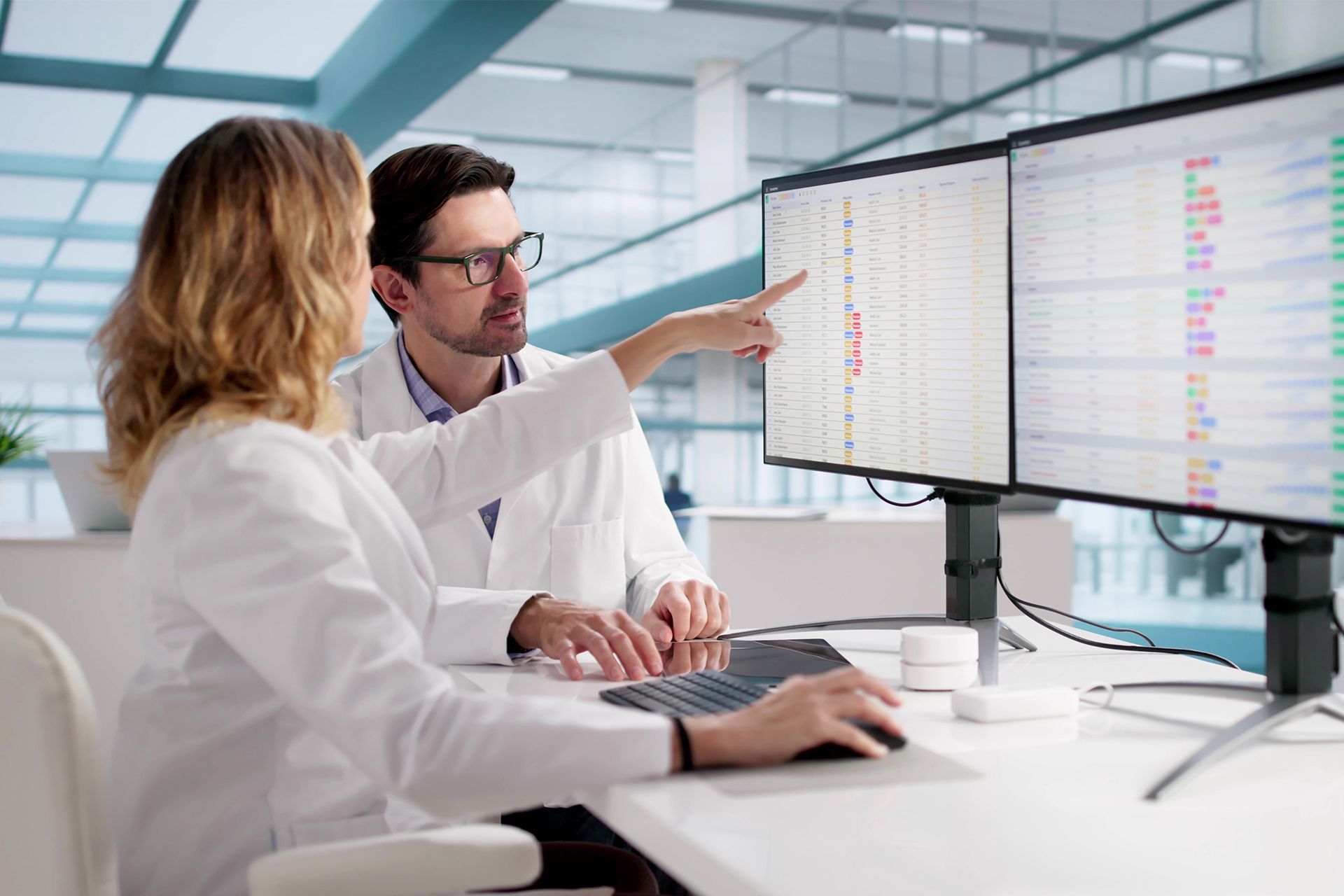 Two coworkers analyzing data on dual monitors in a modern office