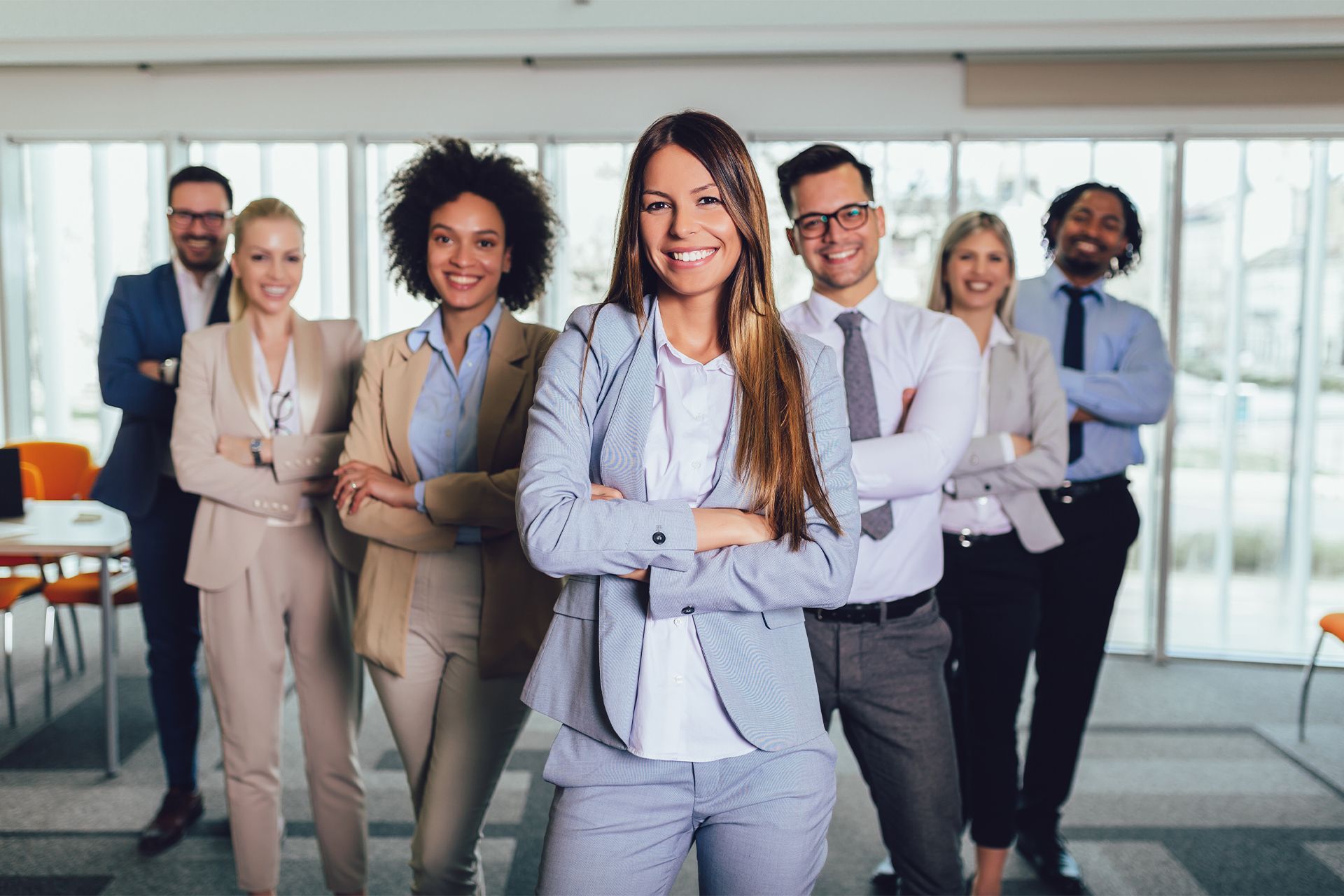 Six business professionals stand smiling in a modern office with arms crossed.