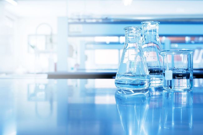 Blue laboratory beakers and flasks on a reflective lab bench, with a blurred science background