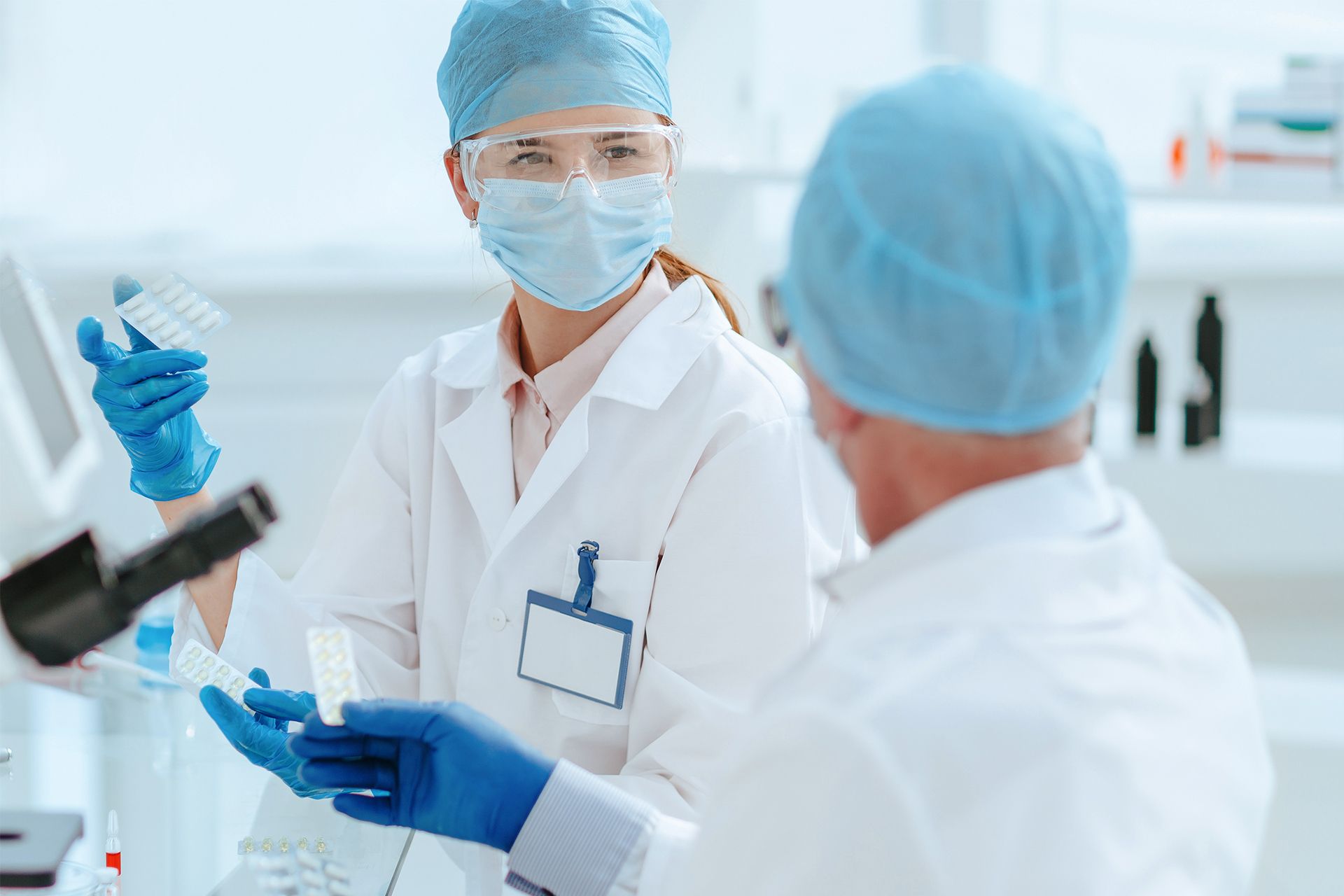 Doctors in lab coats and blue caps discussing research in a bright laboratory